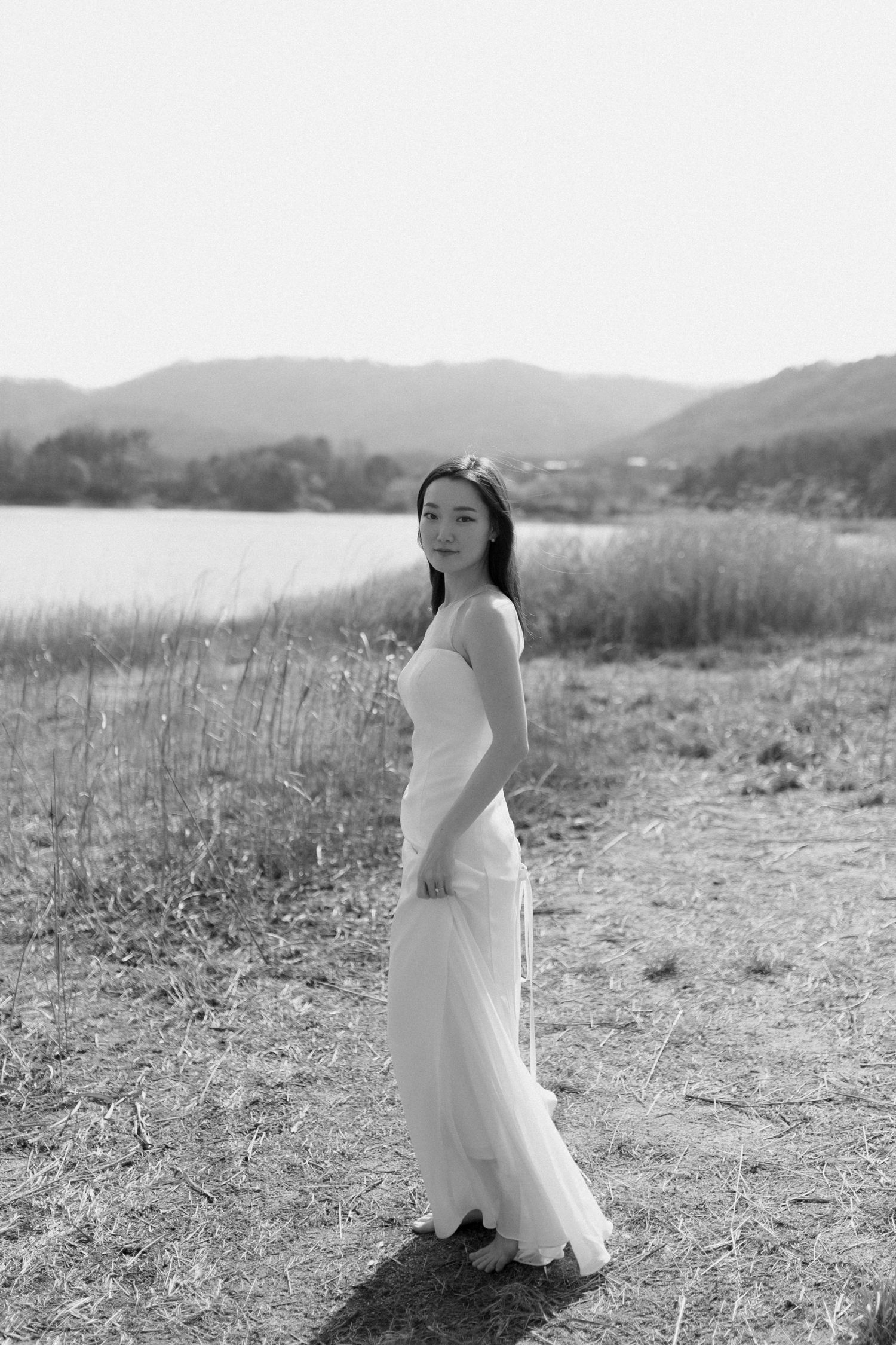 Bride standing by lake with mountains in background during wedding
