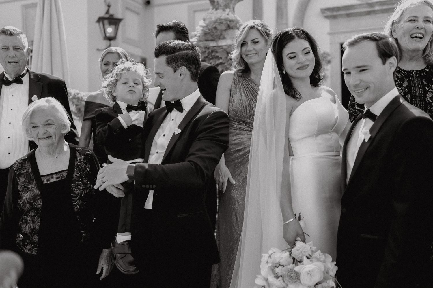 Bride and groom sharing moment with smiling family members outdoors after wedding ceremony