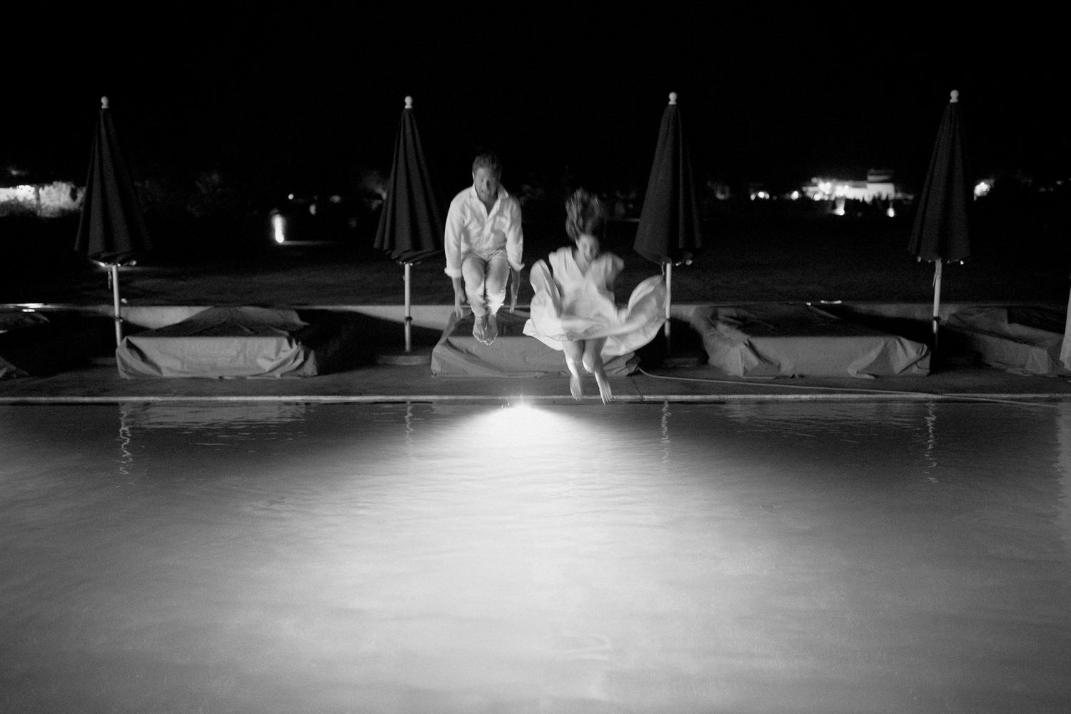 Couple jumping into pool at night during rehearsal dinner