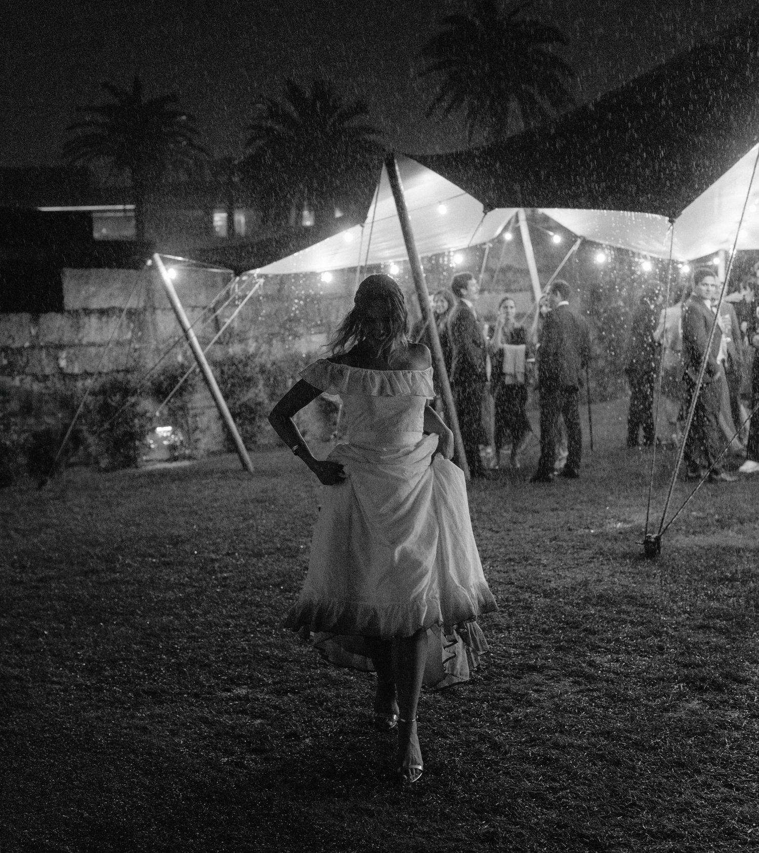 Bride running through rain during outdoor wedding reception in Portugal at night