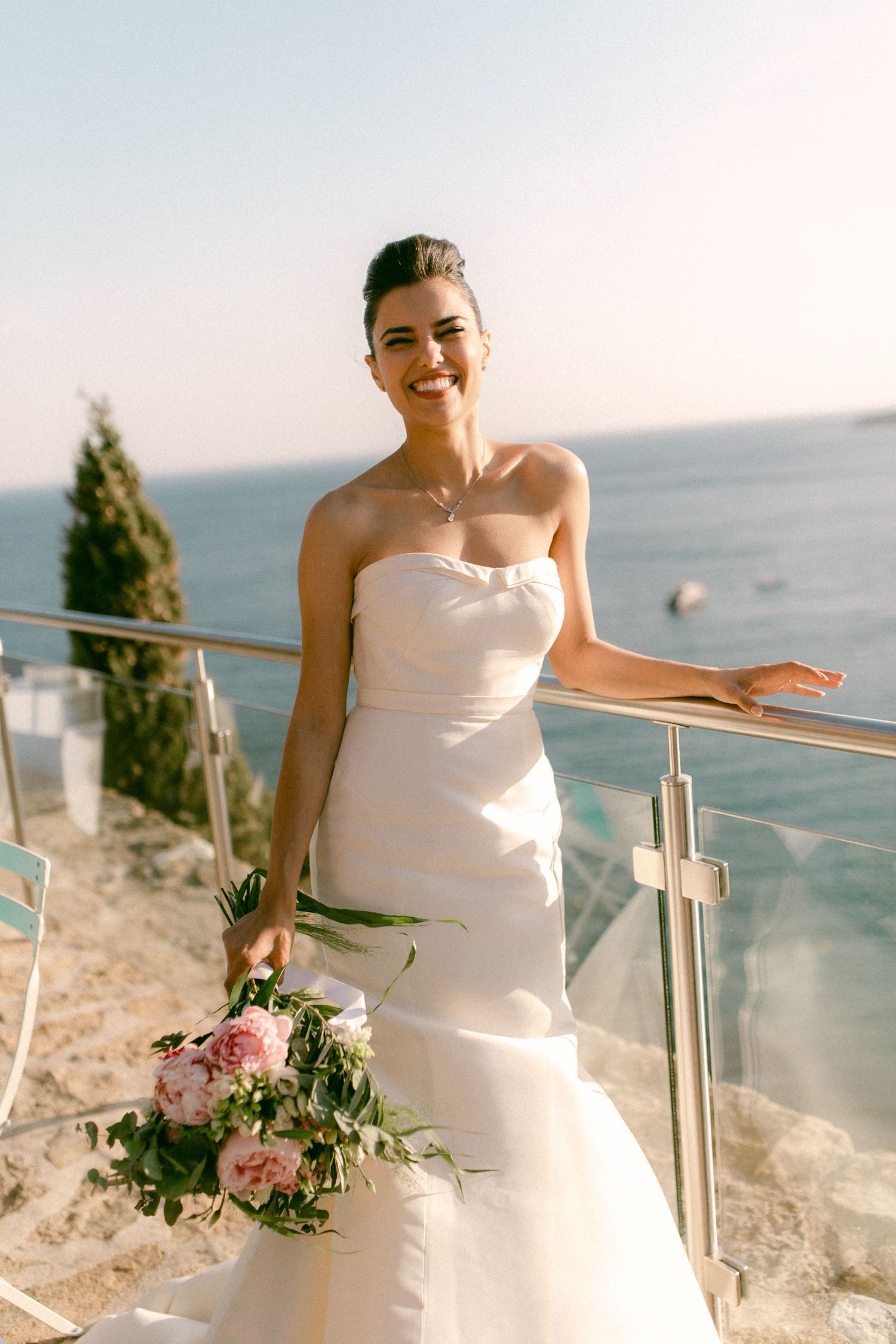 Smiling bride holding pink bouquet on seaside castle balcony in Cassis, France