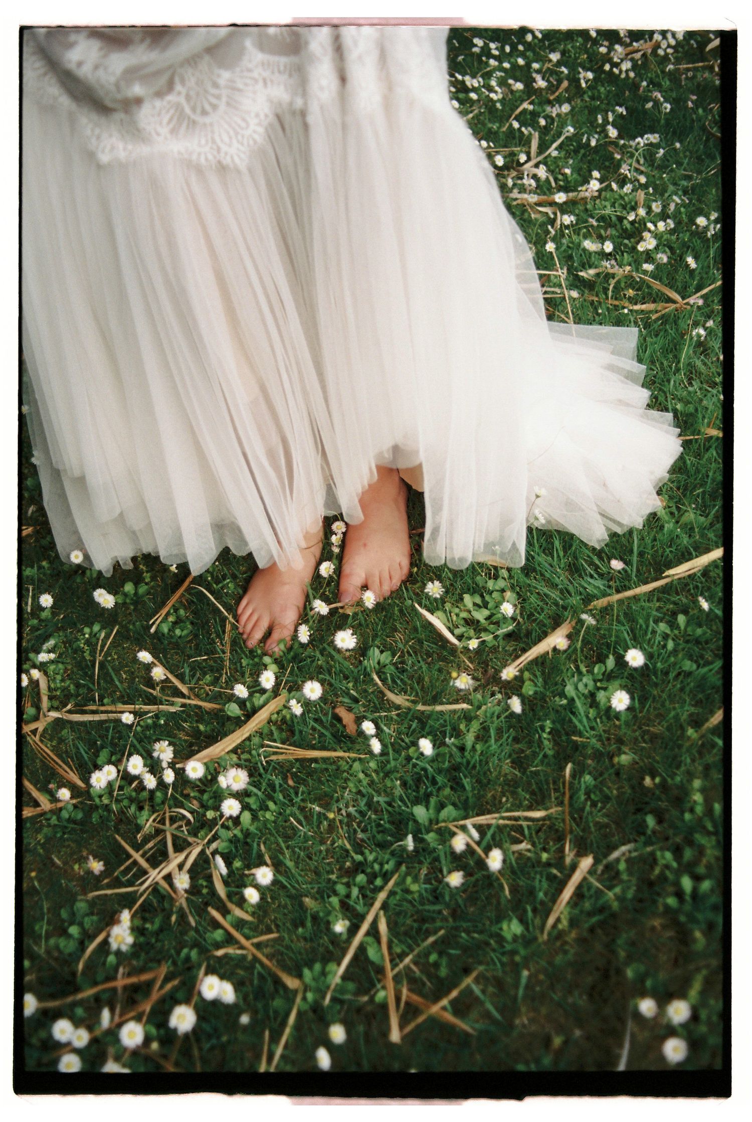 Bride standing barefoot in wedding dress on grass during outdoor celebration