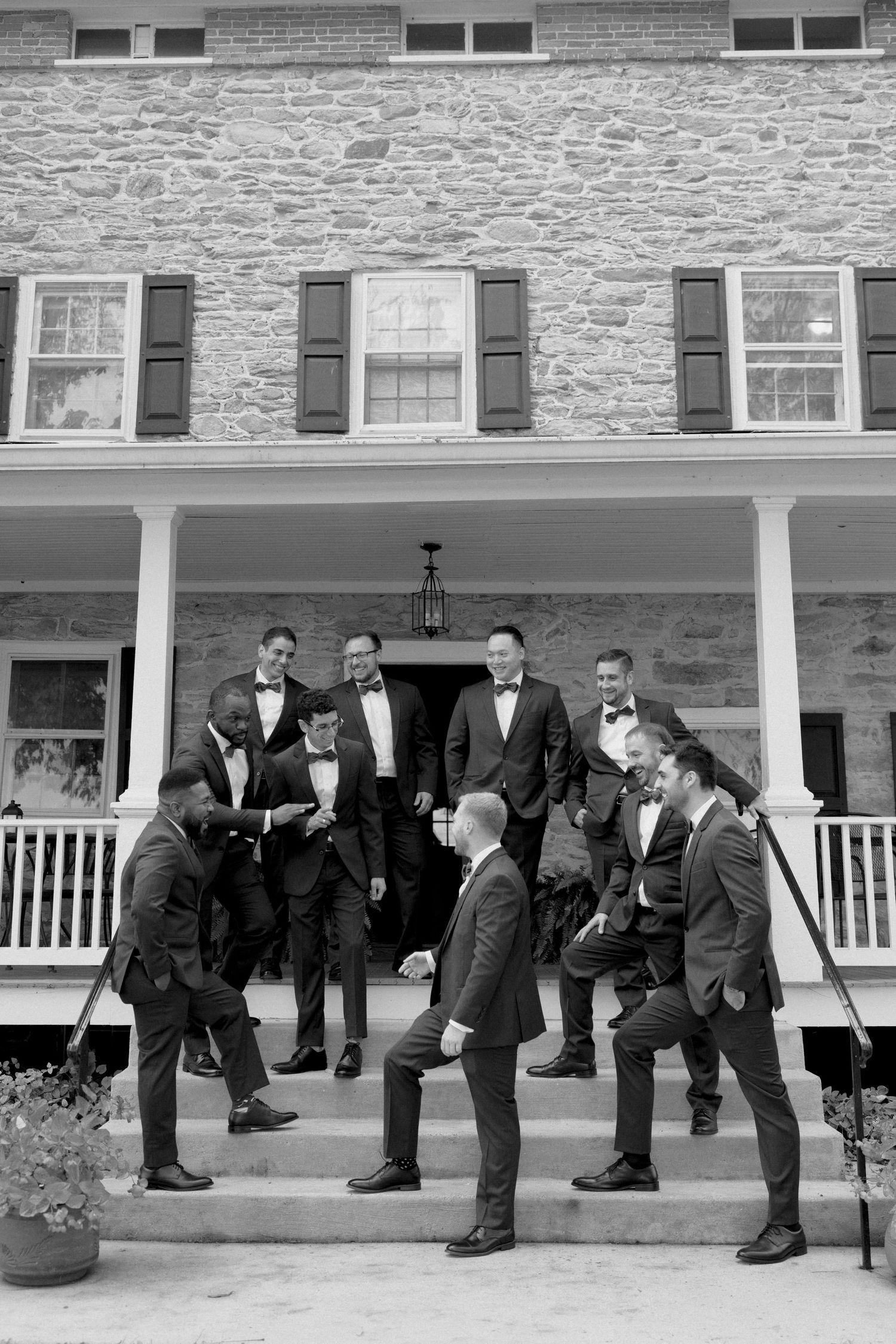 Groom and groomsmen laughing on steps of historic stone building before wedding ceremony