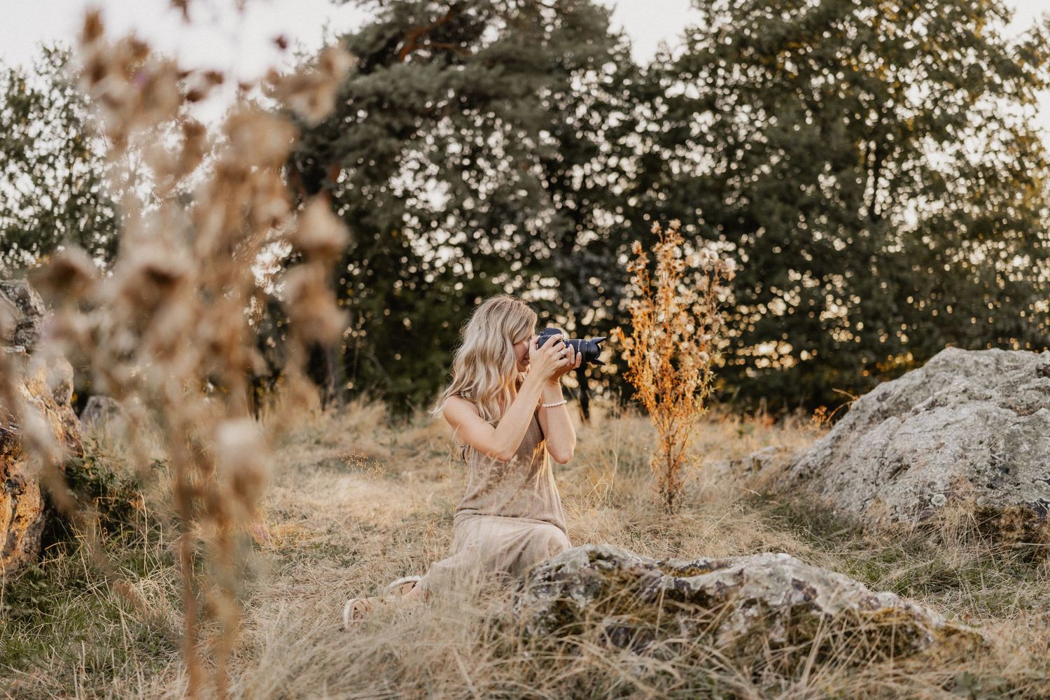 Fotografin auf Stein sitzend im hohen Gras im Sommer fotografiert