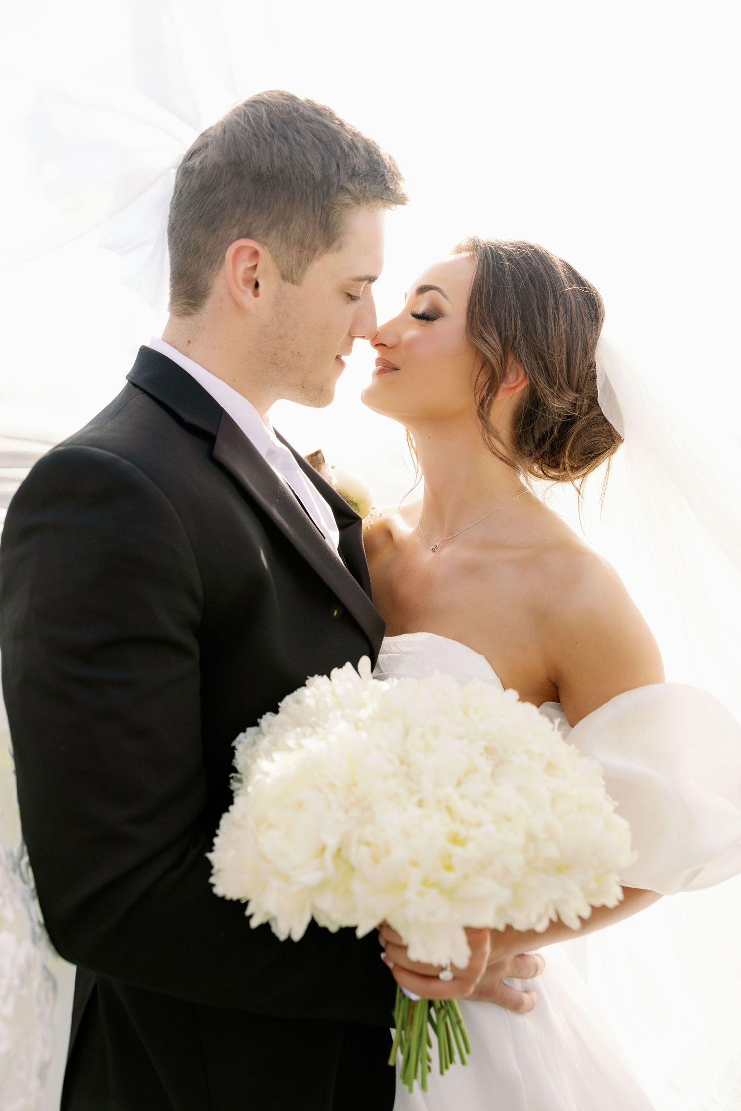 A romantic wedding moment with a couple embracing while holding a luxurious white peony bouquet.