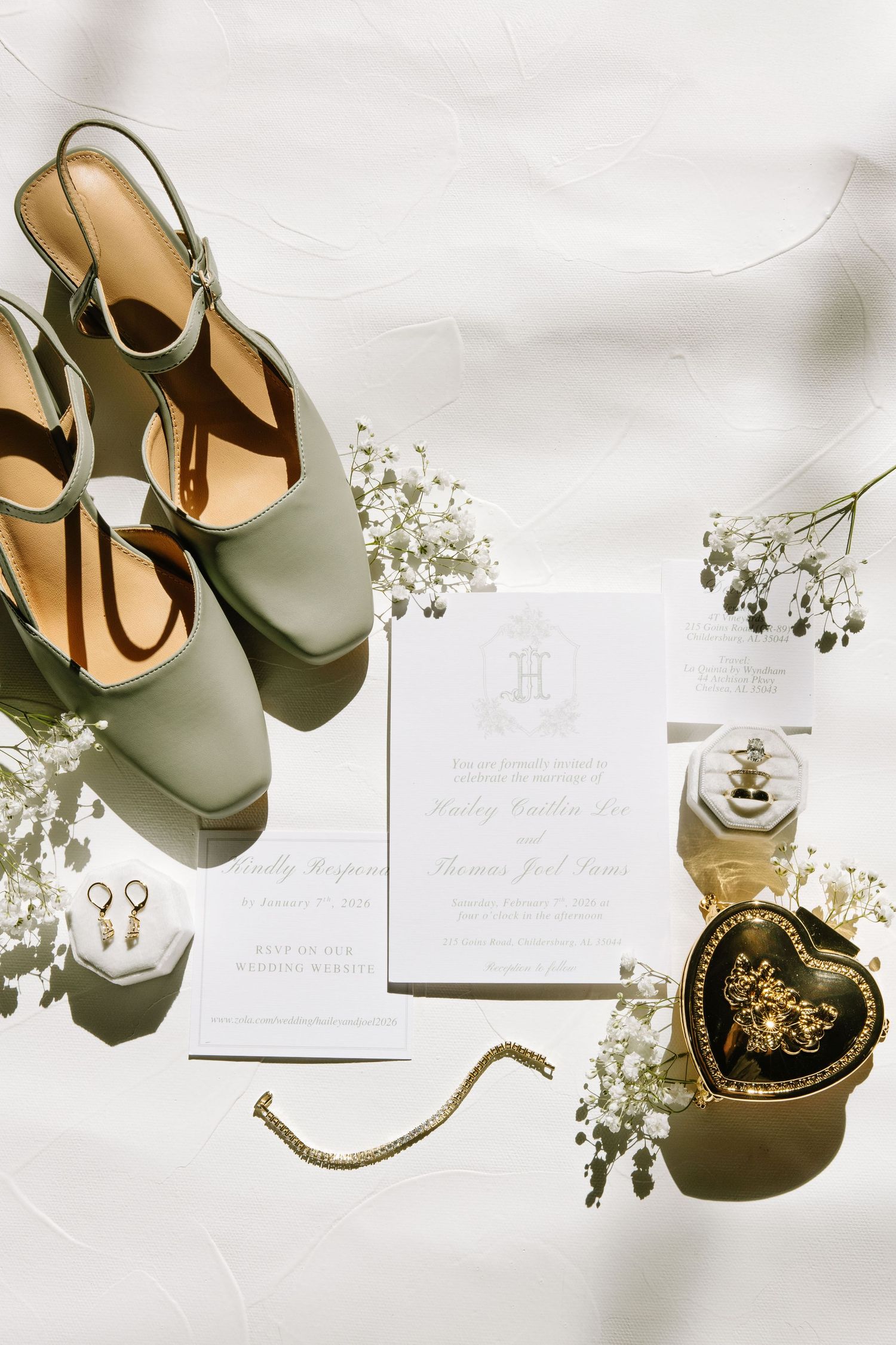Wedding details flatlay with sage green shoes, invitations, and baby's breath flowers.