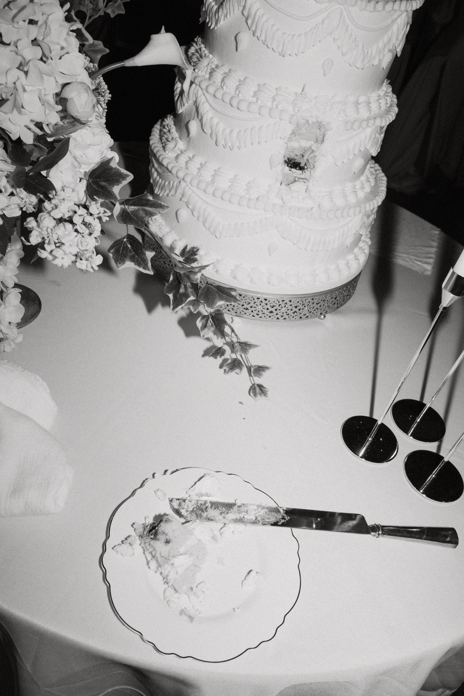 Black and white overhead view of tiered white wedding cake with a slice cut on a plate nearby.
