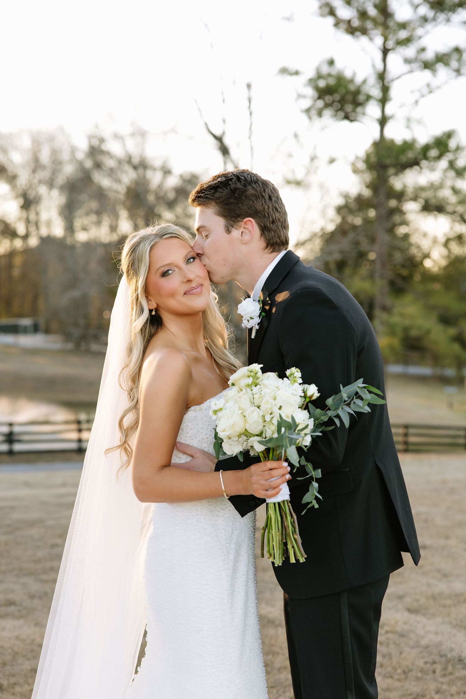 A tender wedding portrait of a couple with white bouquet during golden hour.
