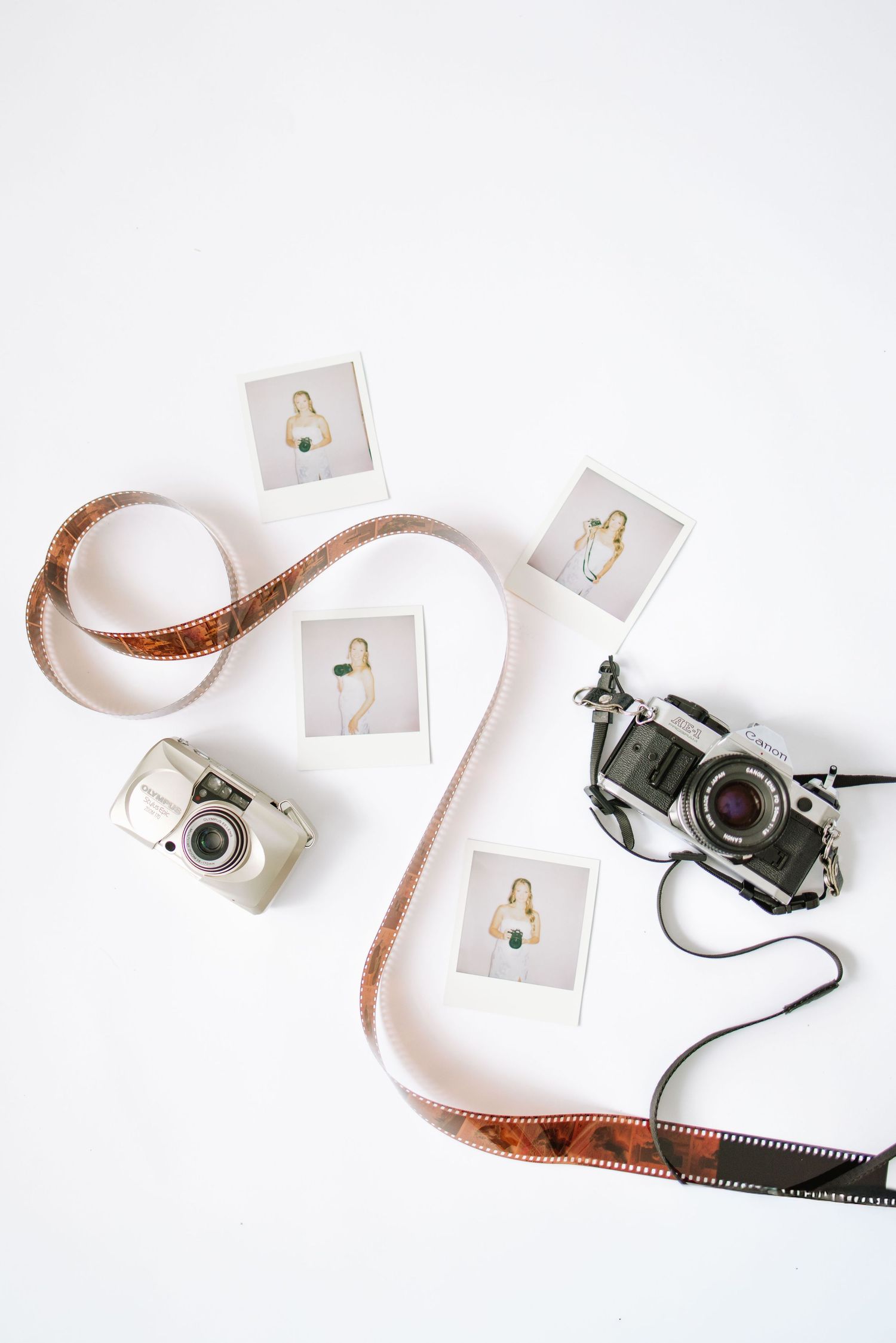 Flat lay of two vintage film cameras, photo film strips, and Polaroid photos on a white background.