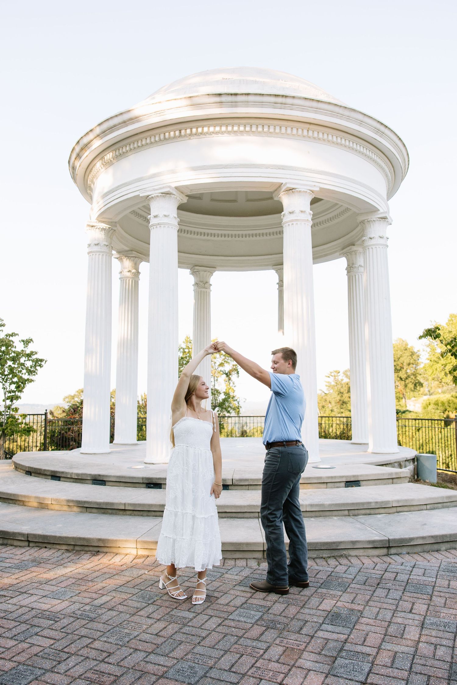 Couple dancing romantically in front of a white classical rotunda with columns in an outdoor garden setting.