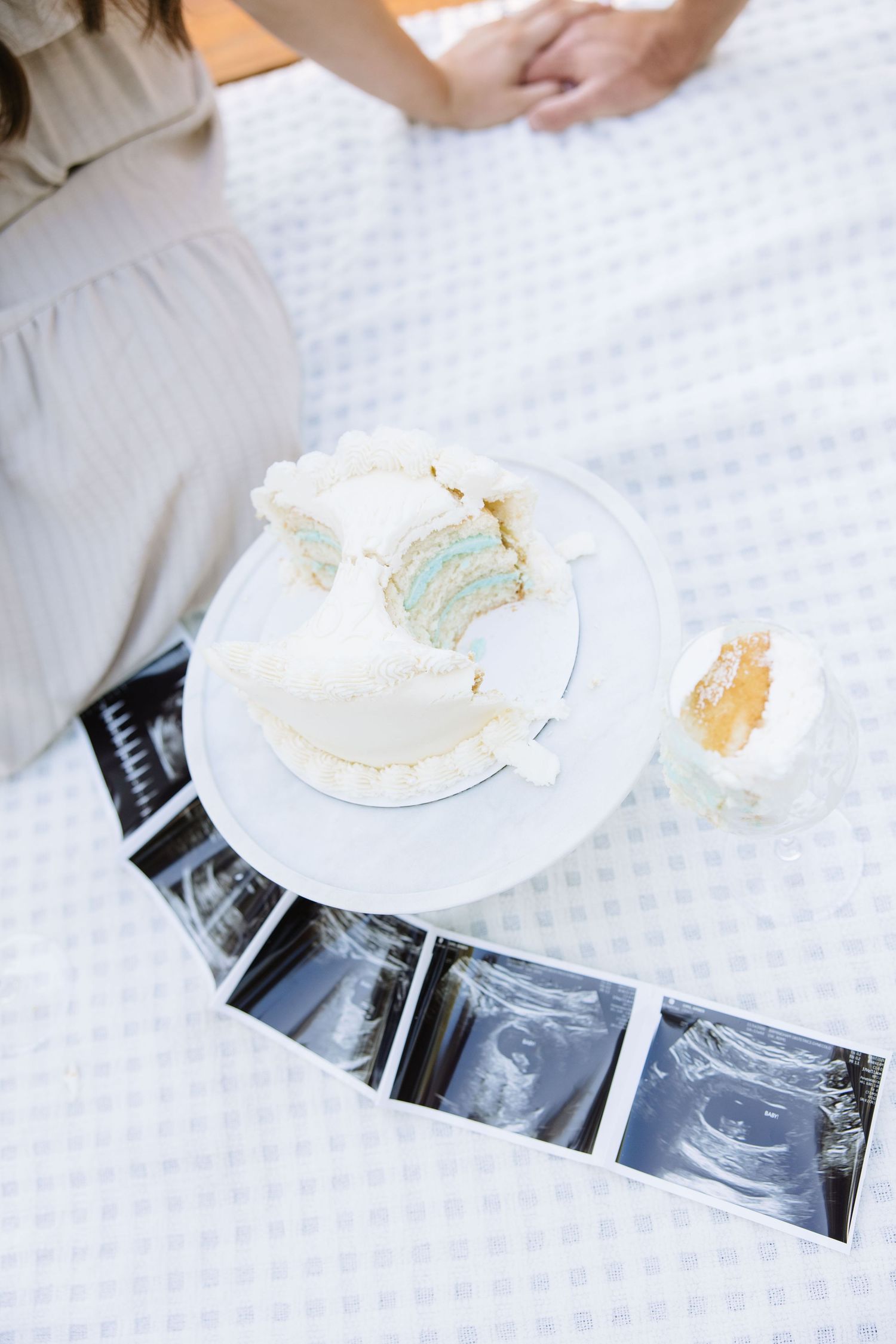 Gender reveal cake with blue interior surrounded by ultrasound photos on a bed, celebrating a baby boy announcement.