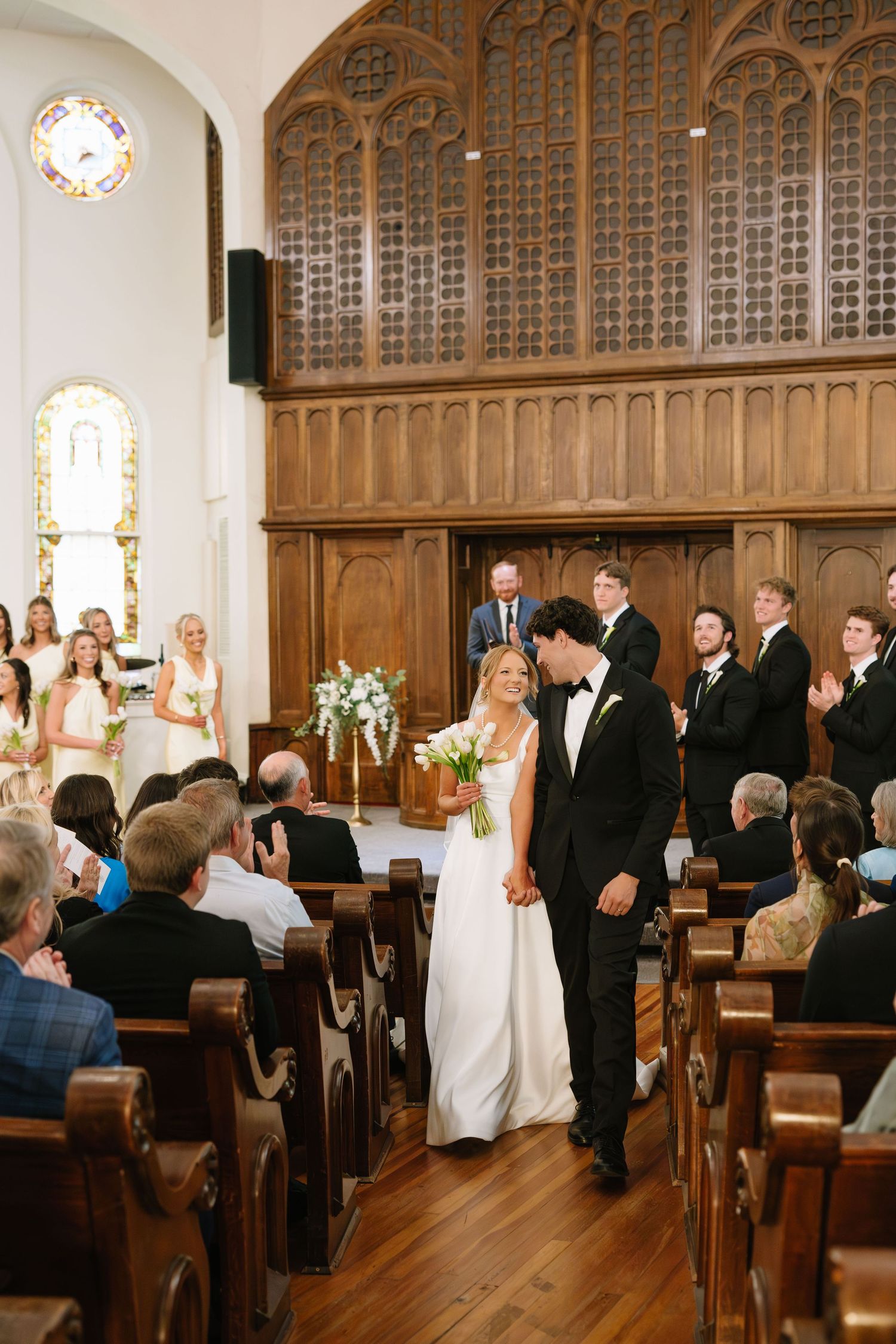 Newlyweds walk down the aisle of an elegant church as guests applaud their ceremony exit.