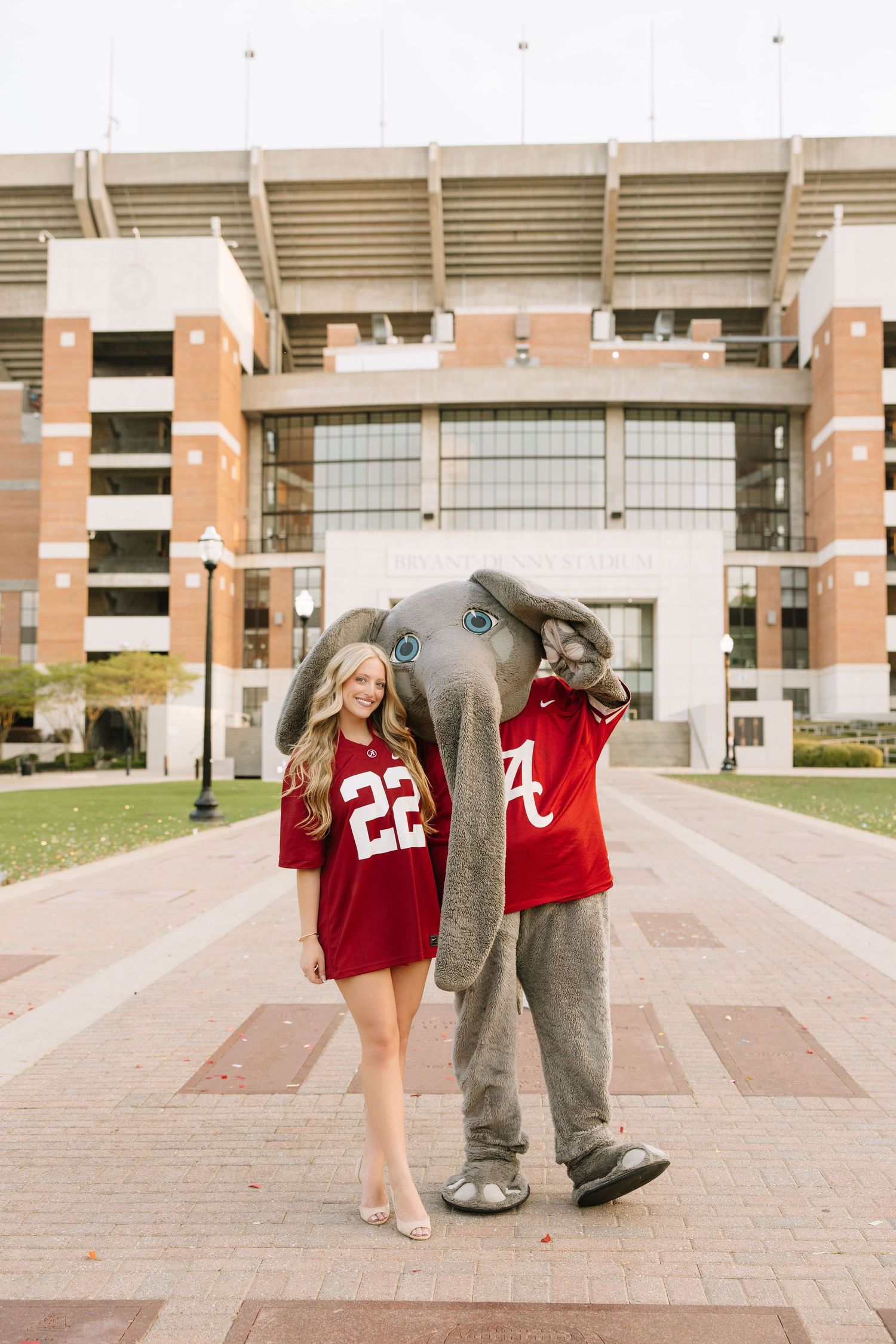 Young woman in Alabama Crimson Tide jersey poses with Big Al elephant mascot outside Bryant-Denny Stadium.