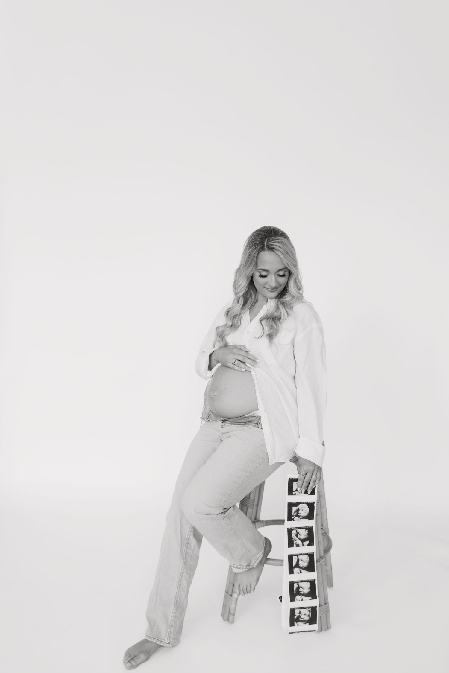 Black and white photo of a pregnant woman cradling her belly, leaning against a strip of ultrasound images.