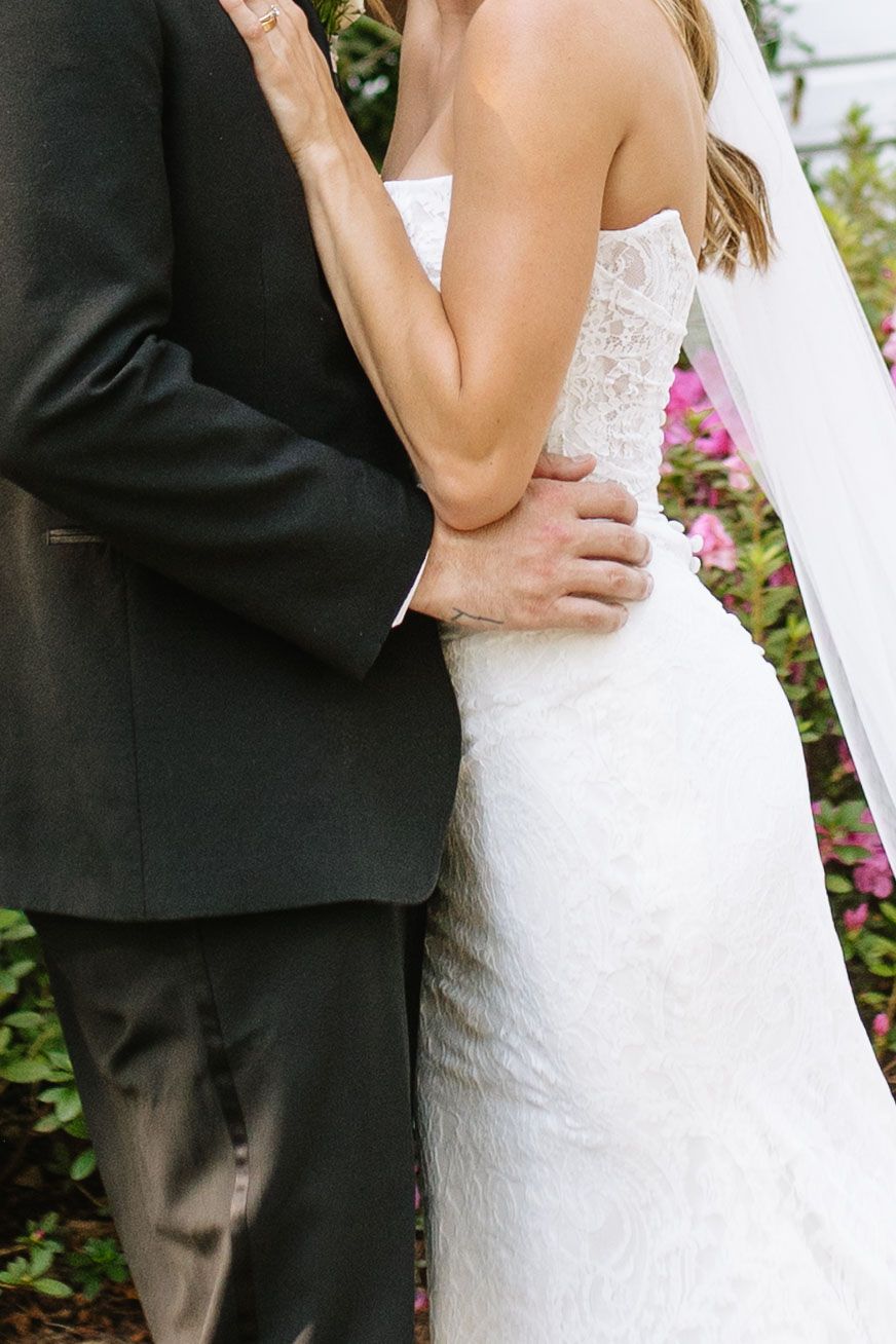 Close up detail of wedding dress lace and black tuxedo as couple embraces.