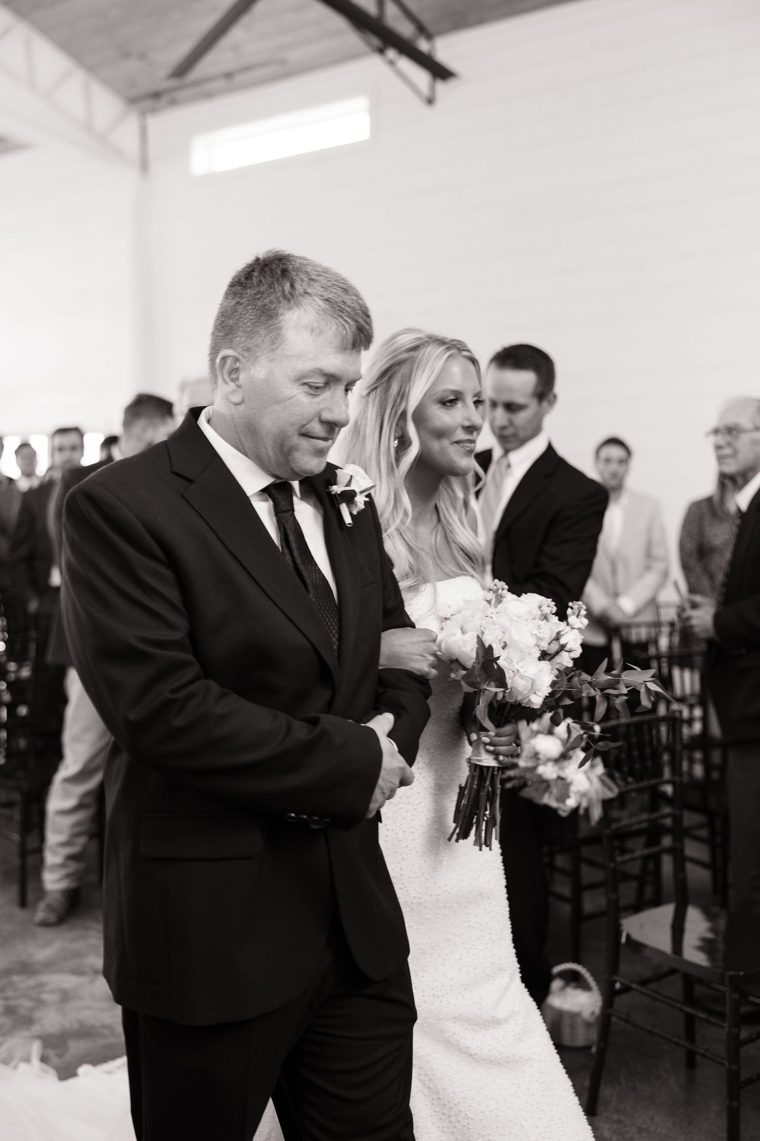 Wedding ceremony processional in a white indoor venue with guests looking on.