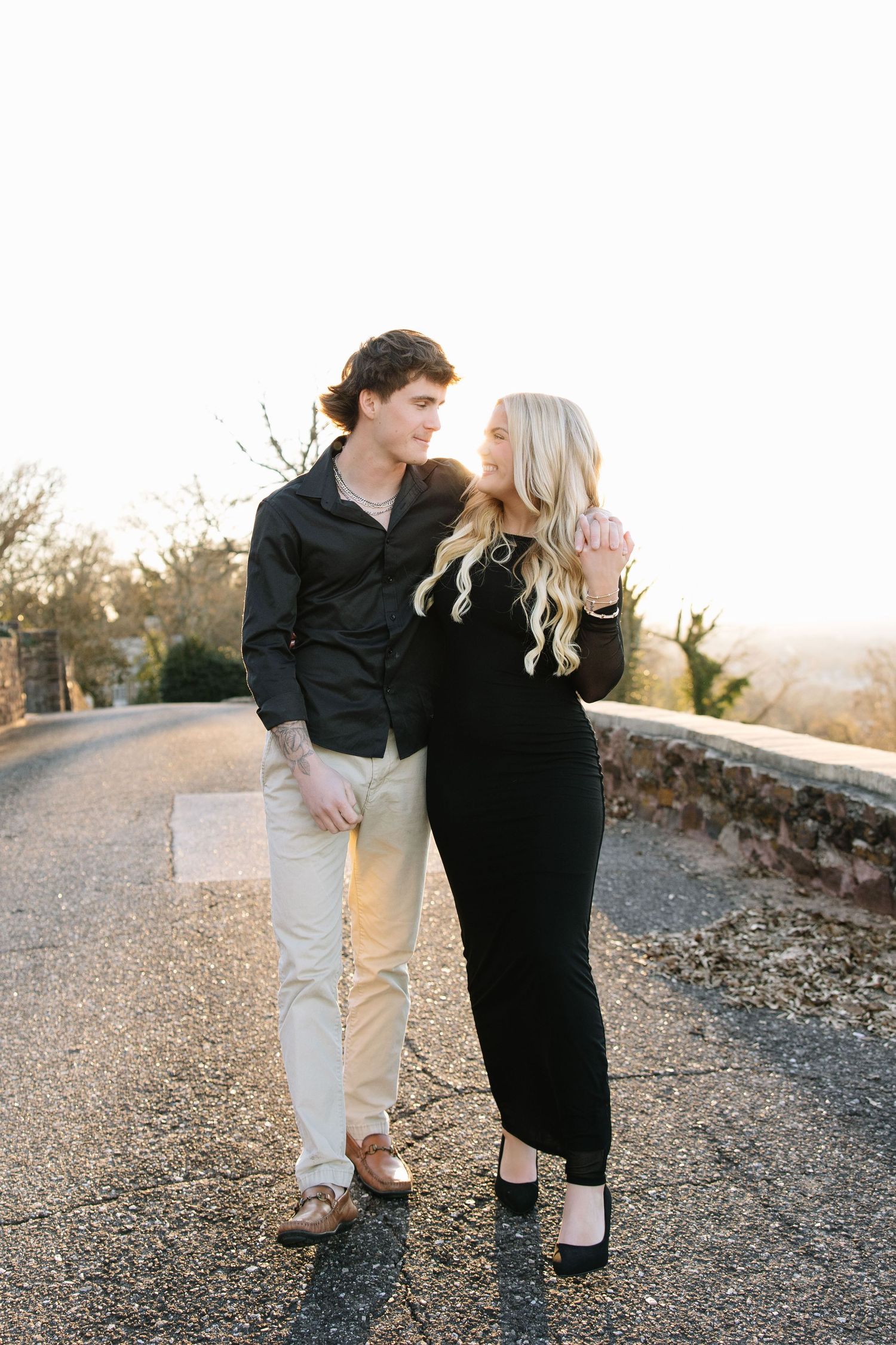 Couple in matching black outfits sharing a romantic moment on a scenic overlook path at golden hour.