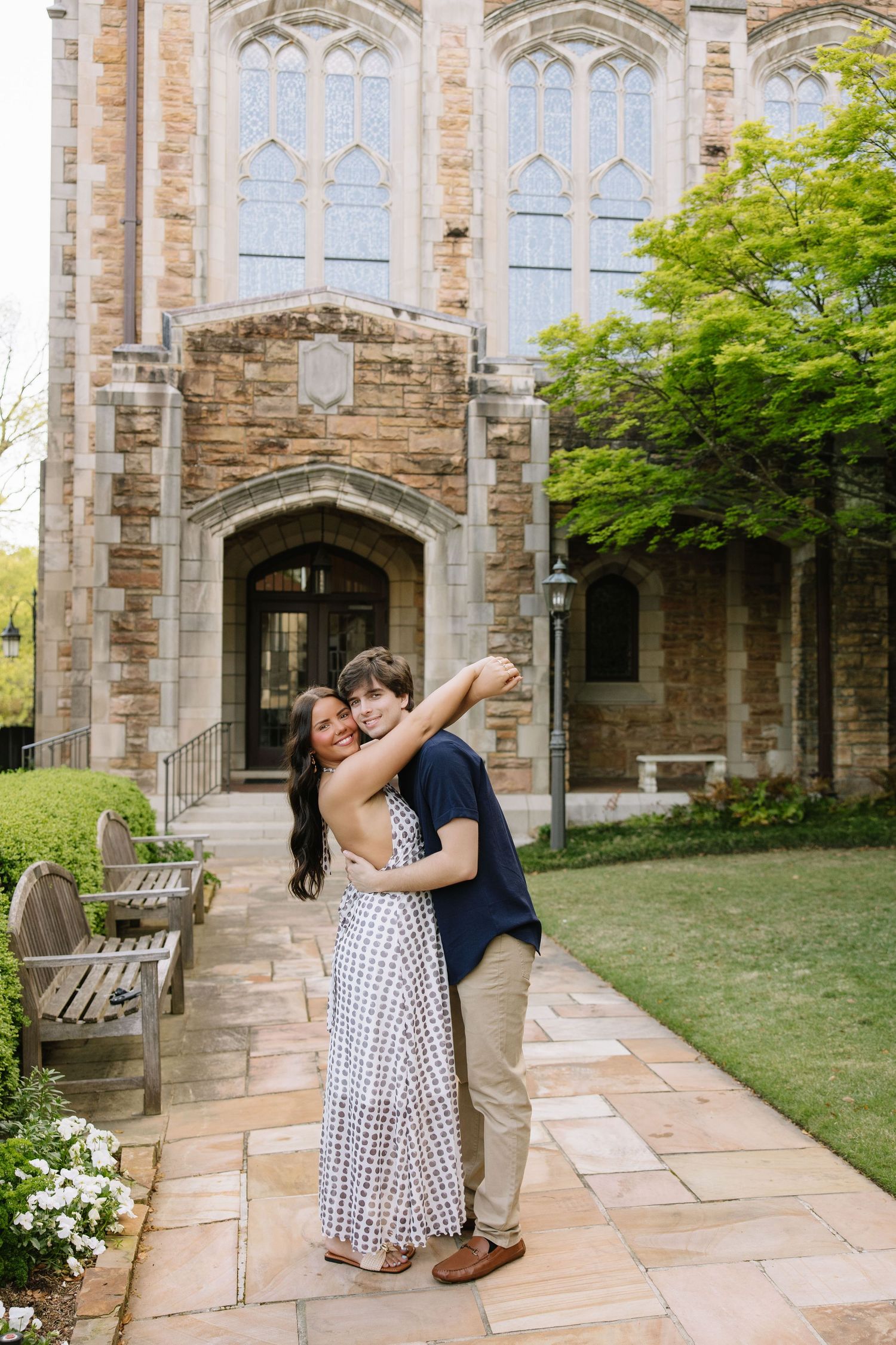 Couple embracing and kissing in front of a stone Gothic church building on a sunny day.