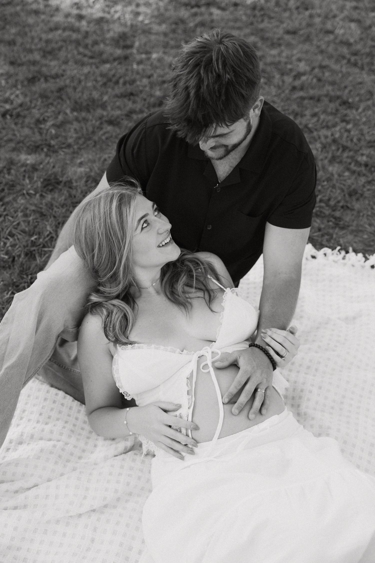 Black and white photo of a couple sitting on a blanket outdoors, woman smiling up at man tenderly.
