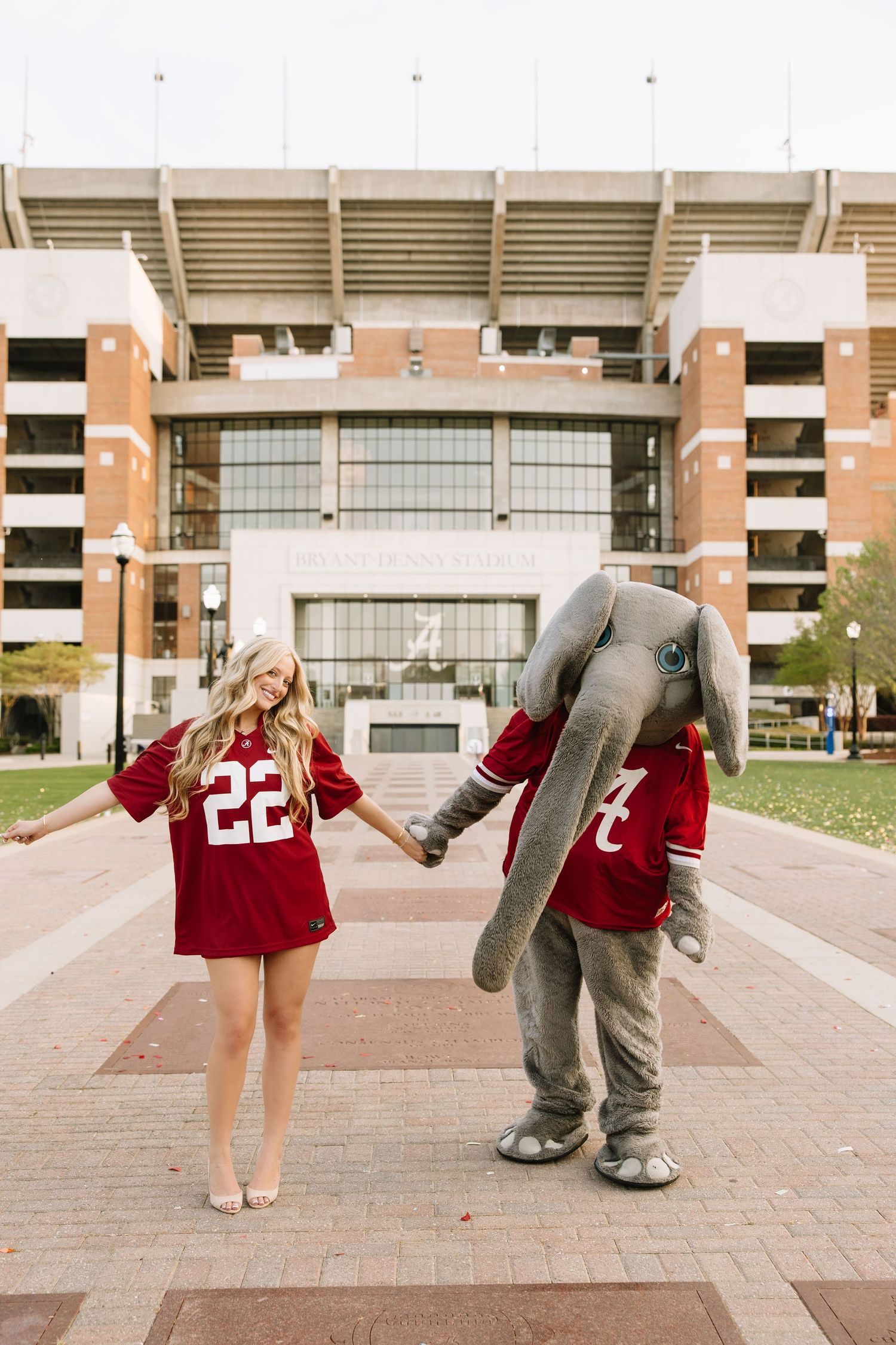 Woman in Alabama Crimson Tide jersey #22 poses with Big Al mascot in front of Bryant-Denny Stadium.