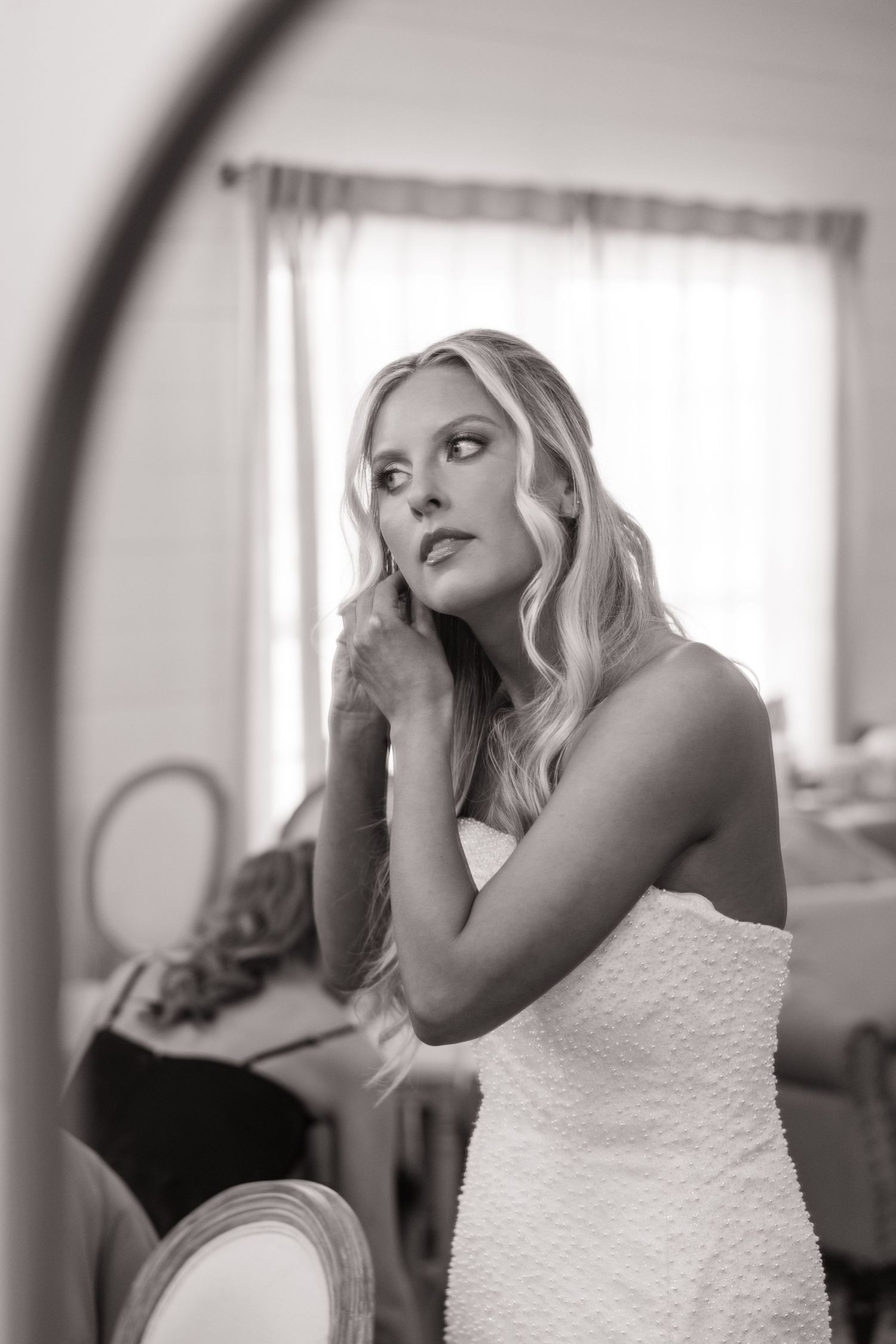 Artistic black and white portrait of a bride getting ready in front of a window.