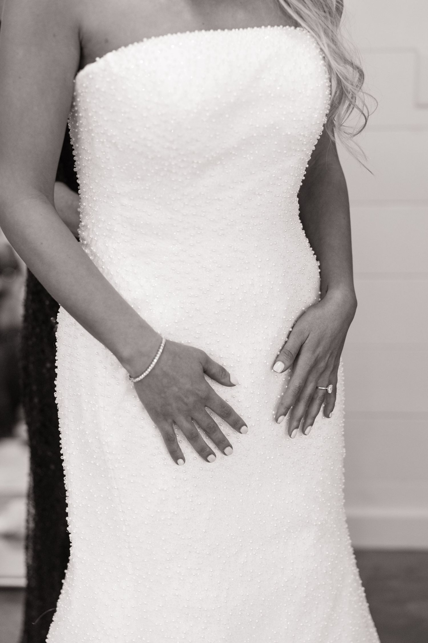 Close-up detail of a strapless beaded wedding gown with bride's hands showing ring.