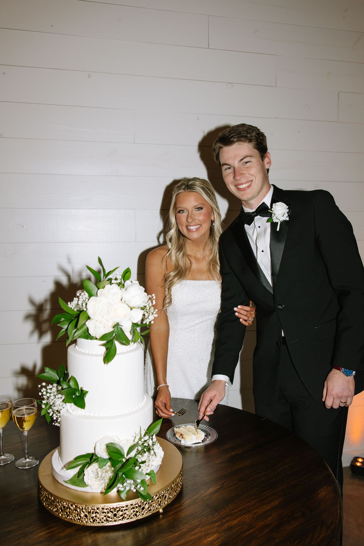 Newlyweds share an intimate moment while cutting their elegant white wedding cake with floral decorations.