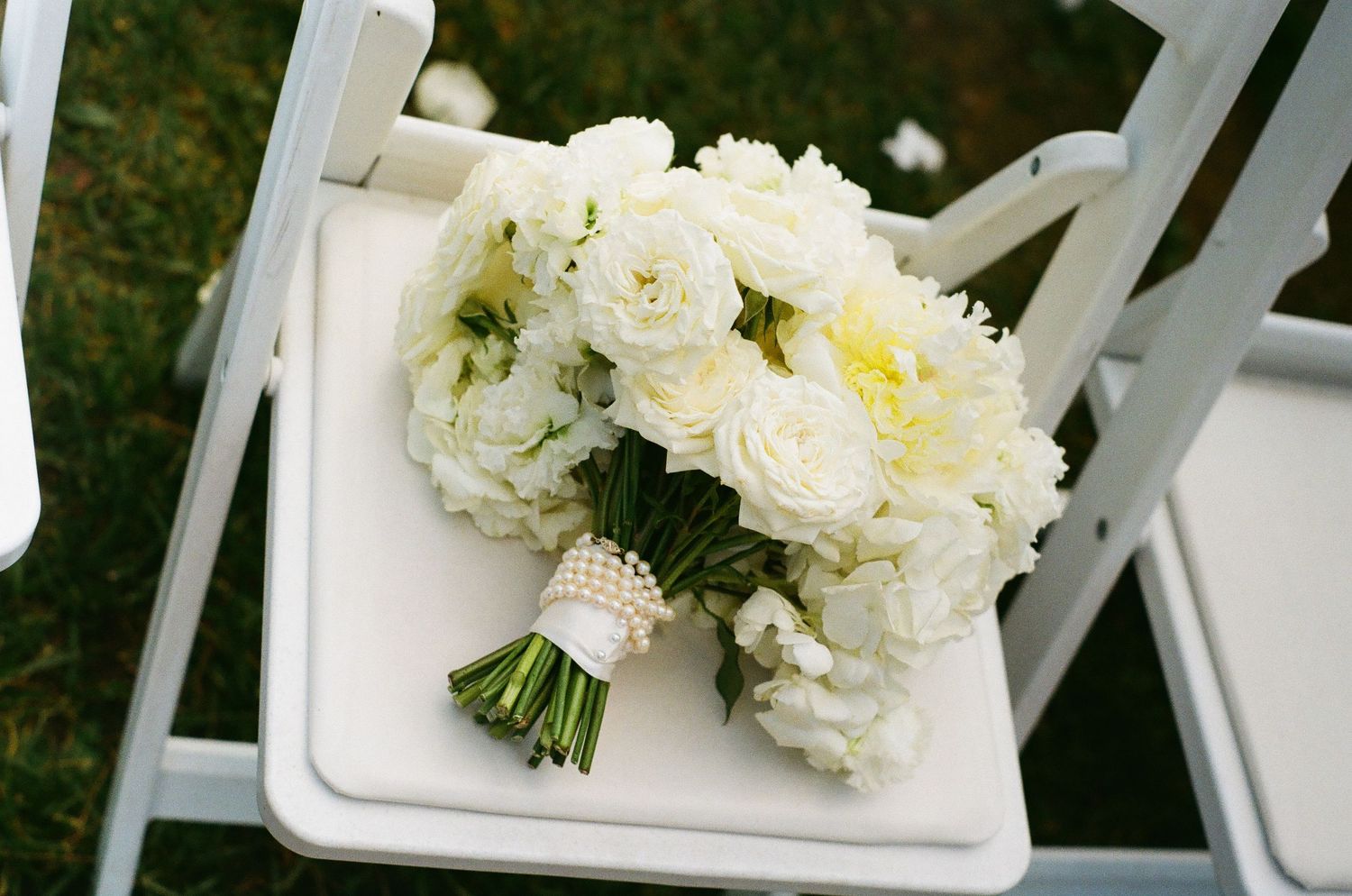 White floral bouquets arranged on white chairs for an outdoor wedding ceremony.