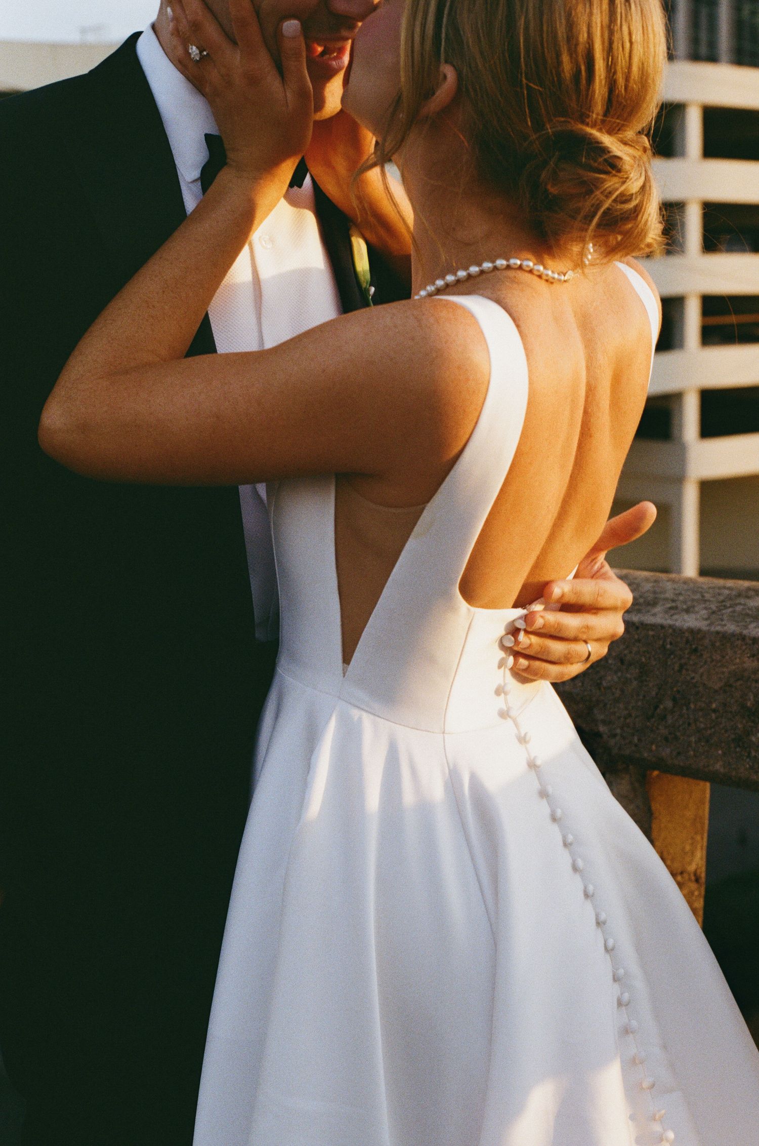 Close-up of bride's elegant backless white wedding gown with pearl necklace and button detail.