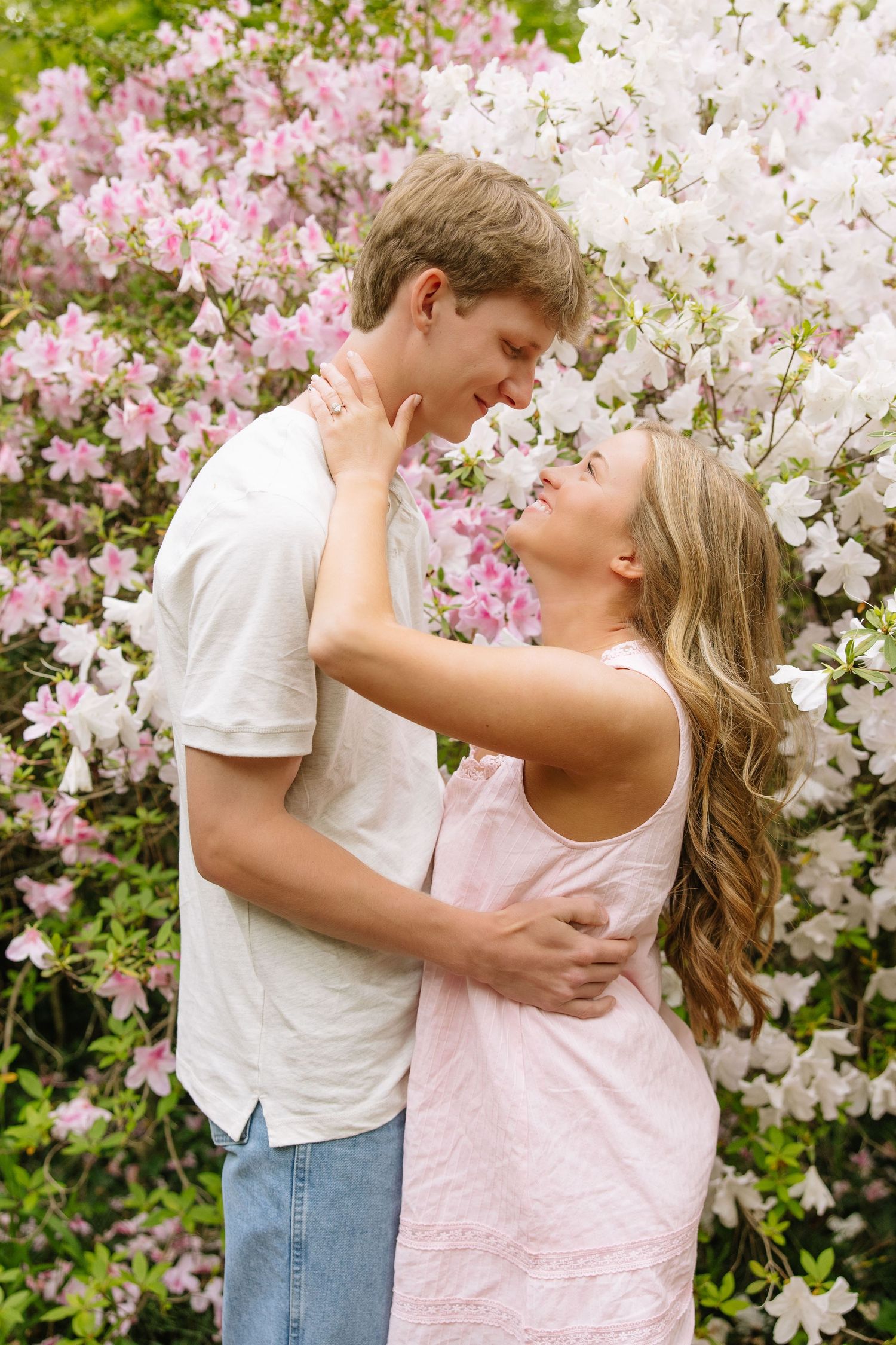 Couple embracing and almost kissing in front of blooming pink and white azalea bushes in spring.