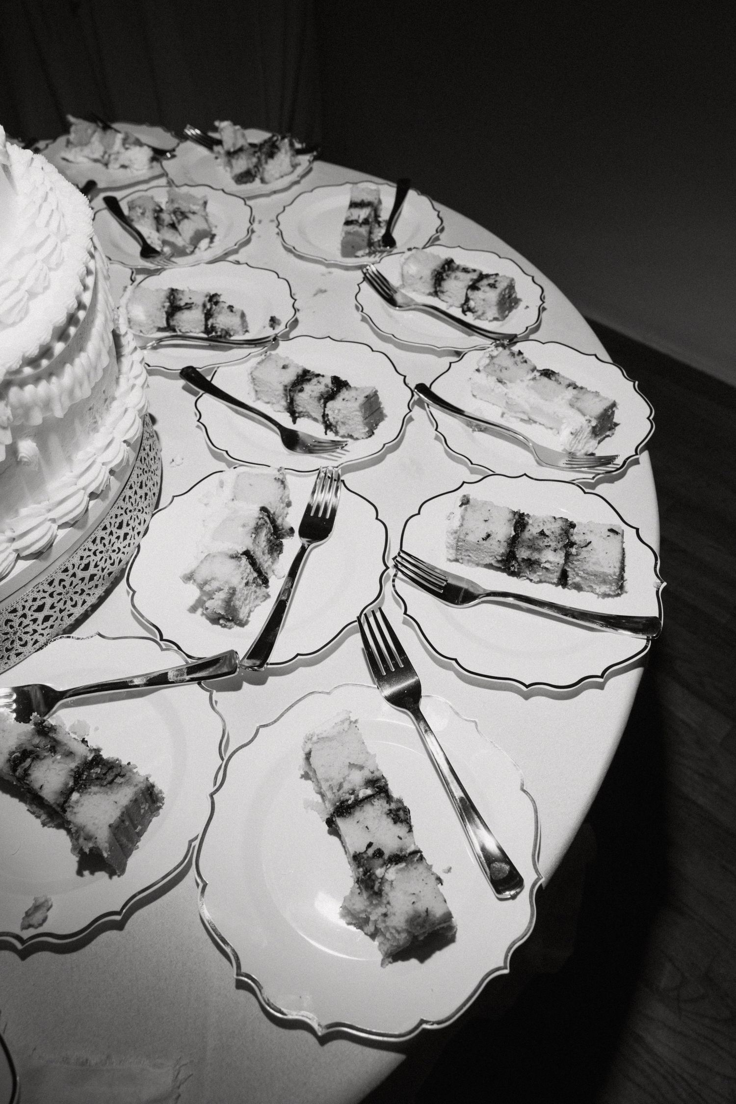 Black and white overhead view of sliced wedding cake pieces plated on decorative dishes with forks on round table.