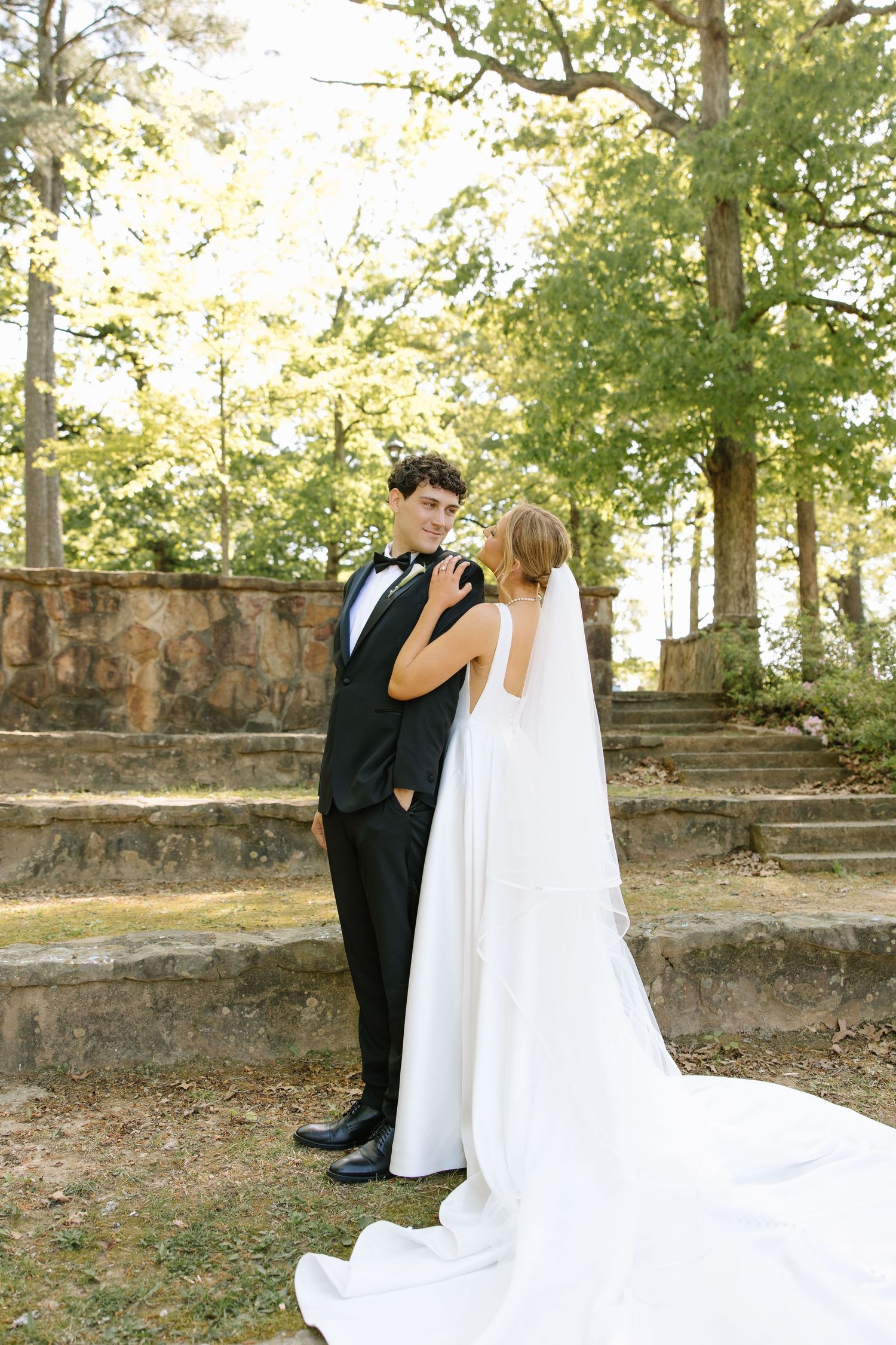 Bride and groom share a tender moment outdoors, with the bride in a flowing white gown and long veil.