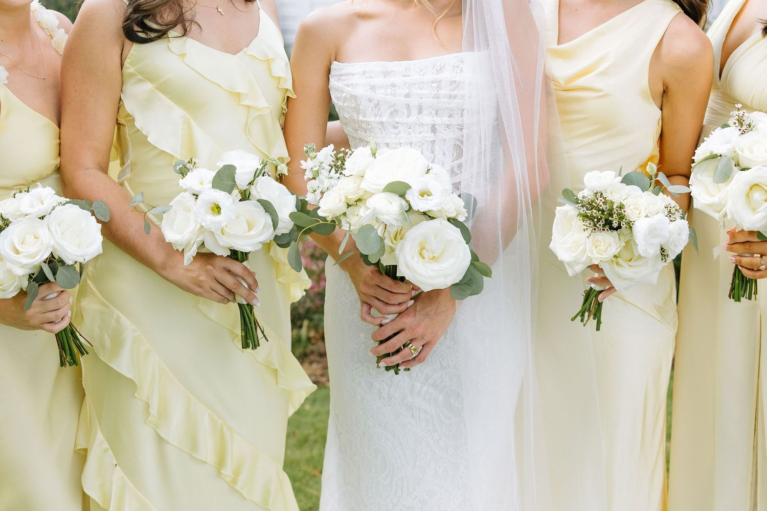 Row of bridesmaids in pale yellow dresses holding white bouquets.
