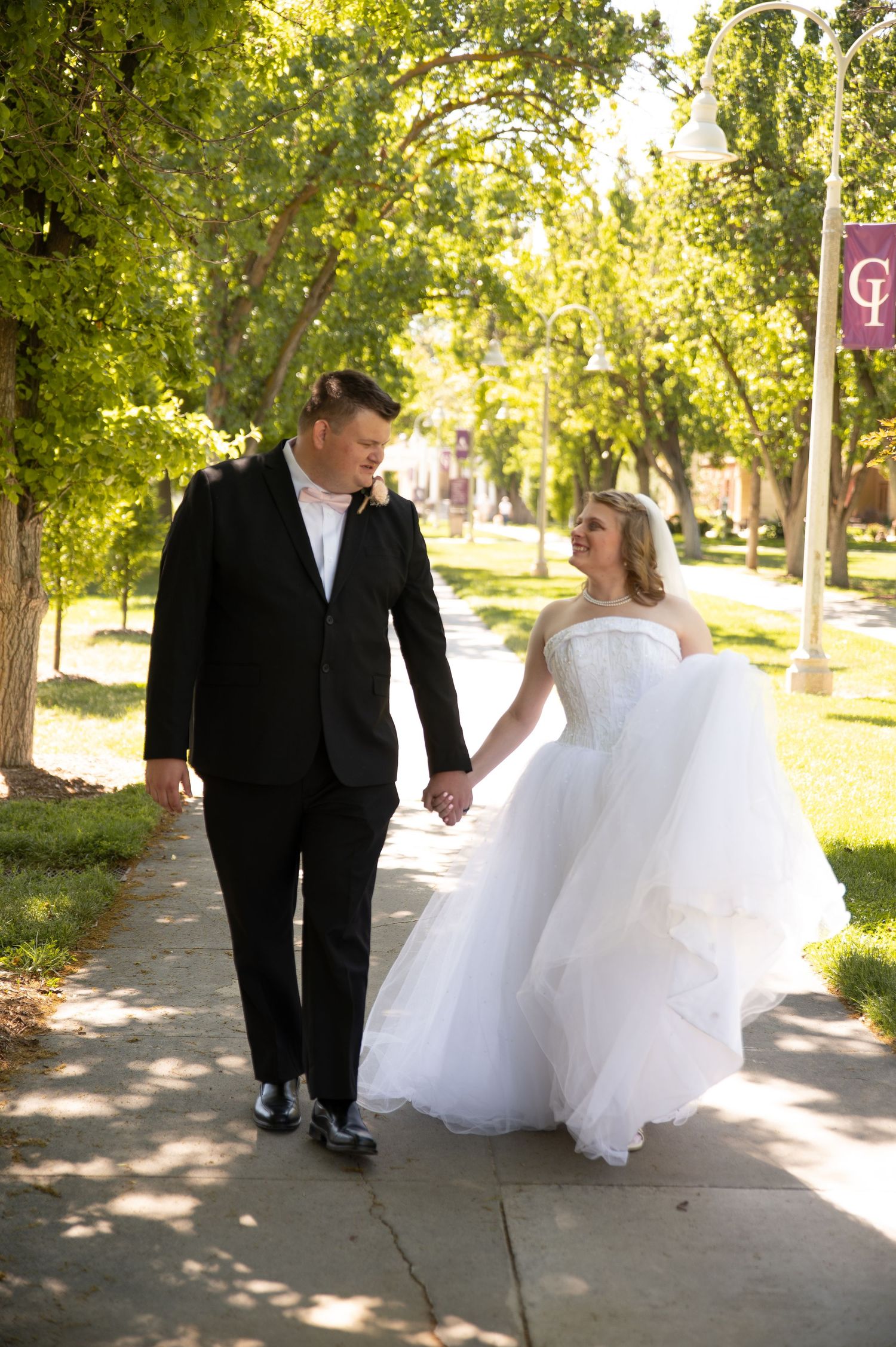 A freshly married bride and groom walk hand and hand on the campus where they met at College of Idaho in Caldwell, Idaho.