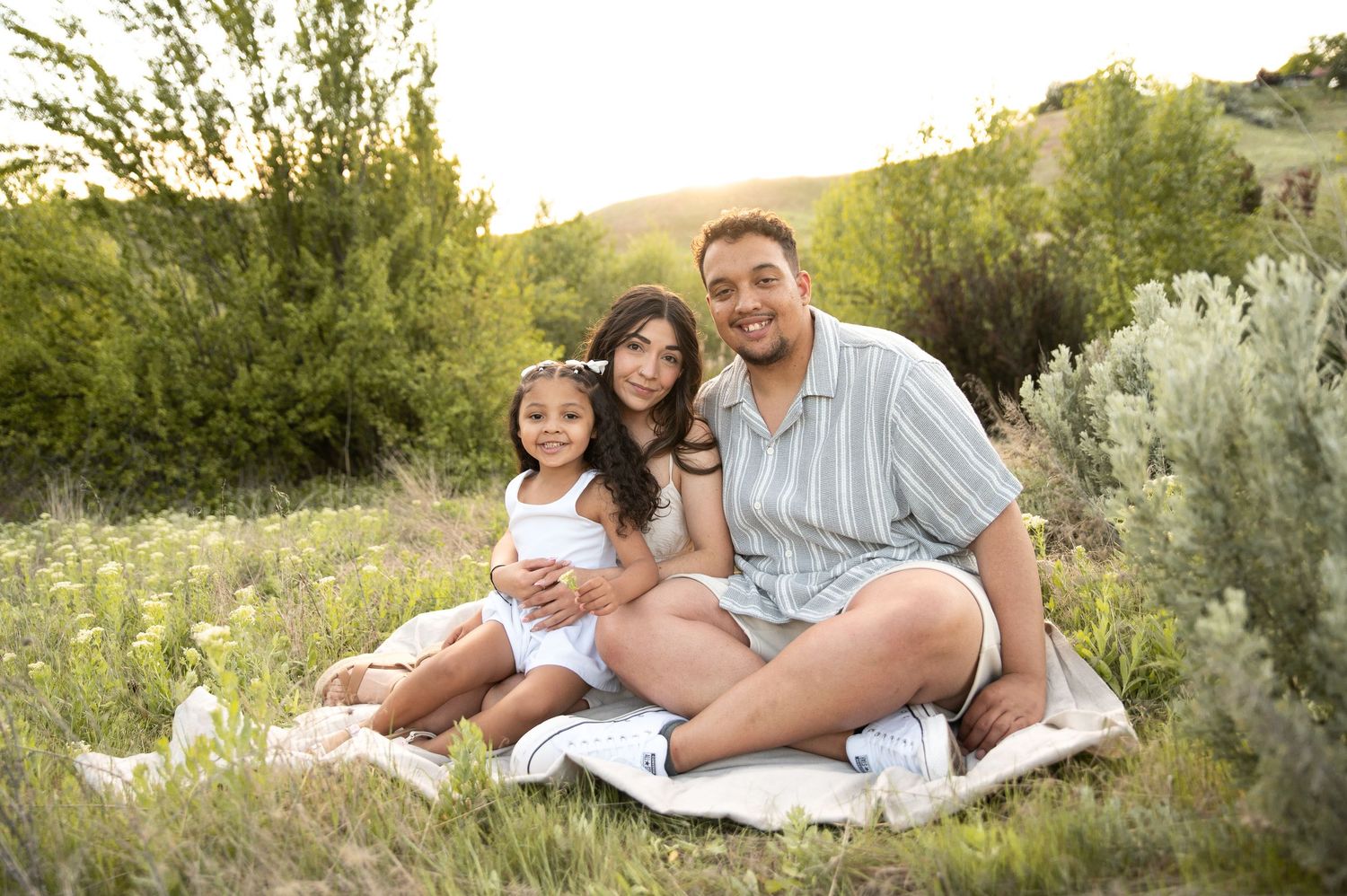 A young family of 3 smiling at sunset in Camels Back Park in Boise, Idaho.