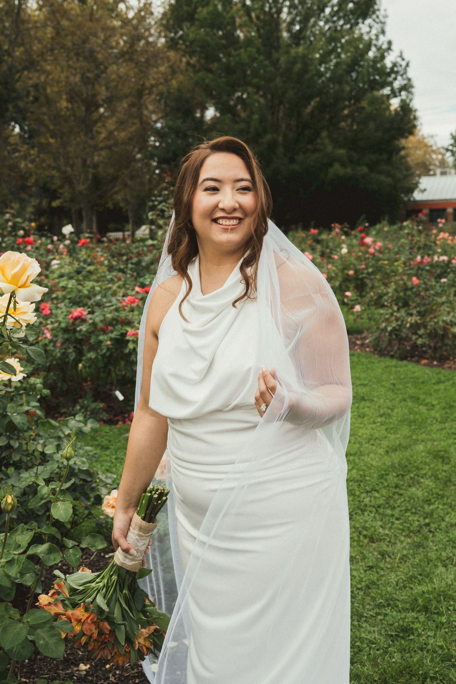 A bride smiling to her groom off camera while surrounding by flowers in the rose gardens of Boise, Idaho.