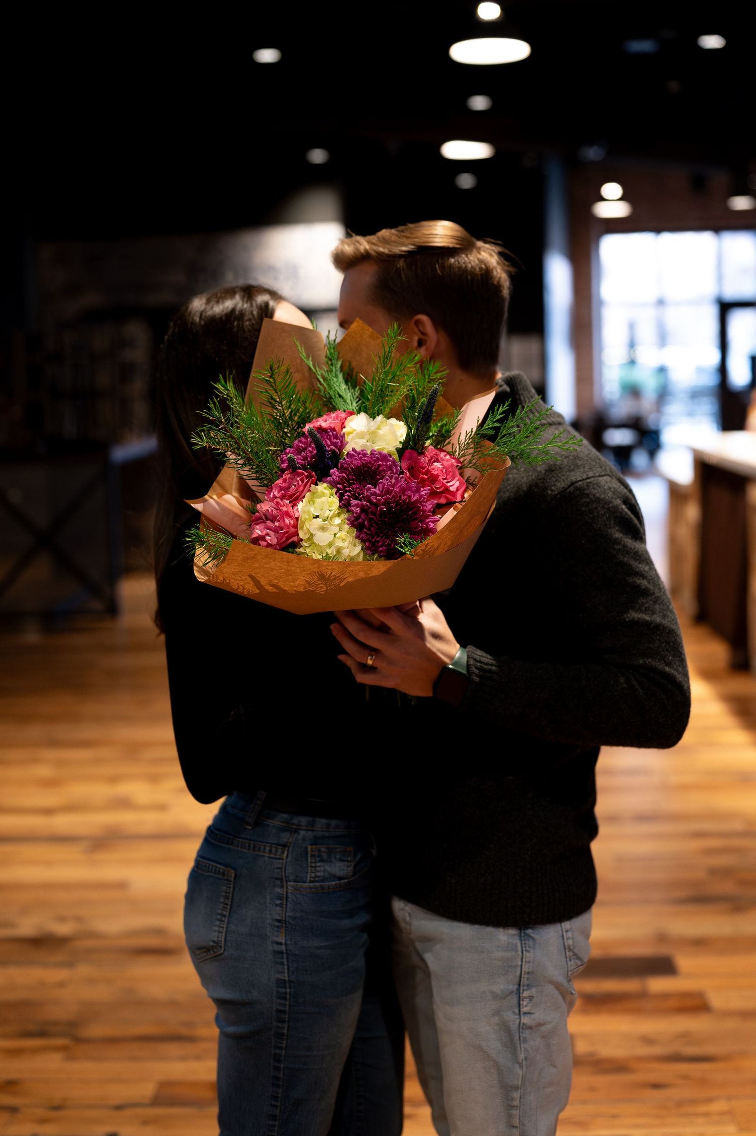 An indoor shot of a couple sharing a kiss behind a beautiful bouquet of flowers in downtown Boise, Idaho.