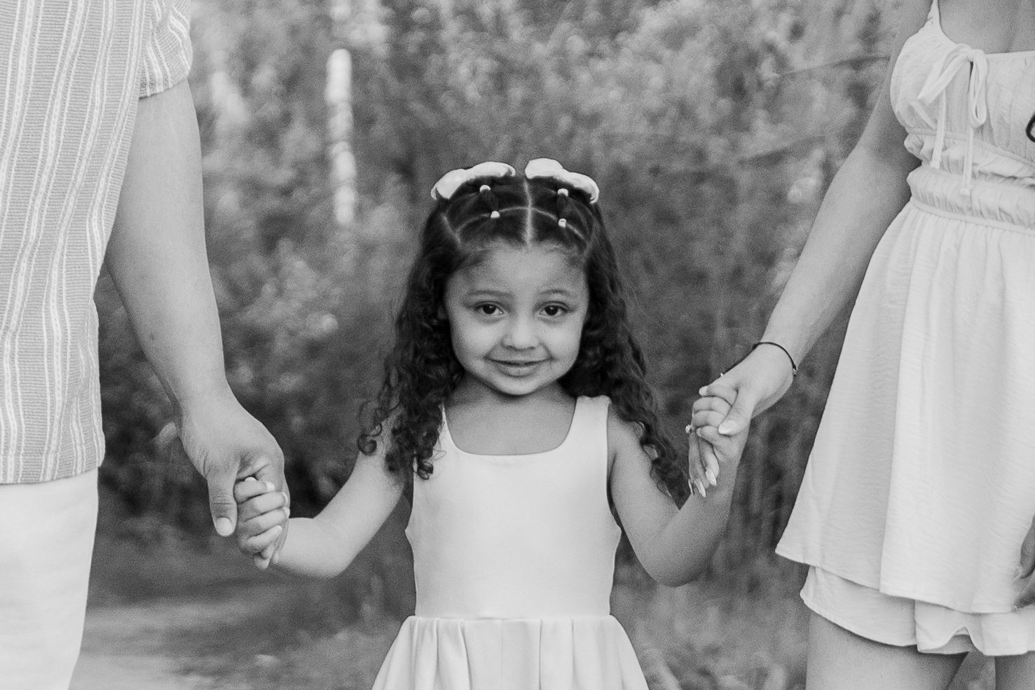 a young girl smiling at the camera while holding her parents hands in boise idaho.