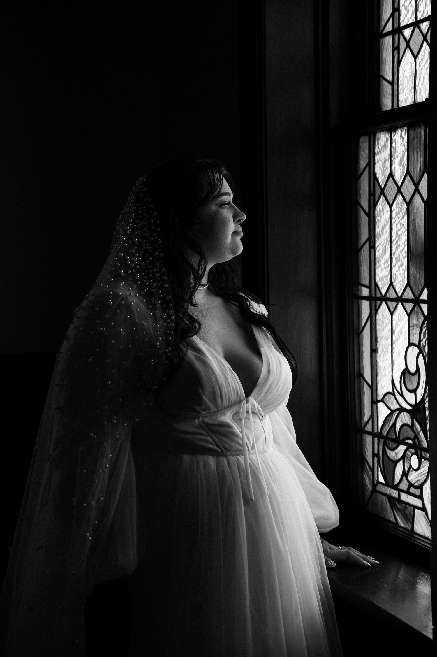 A dark and moody photo of a bride in front of a stained glass church window in Payette, Idaho.