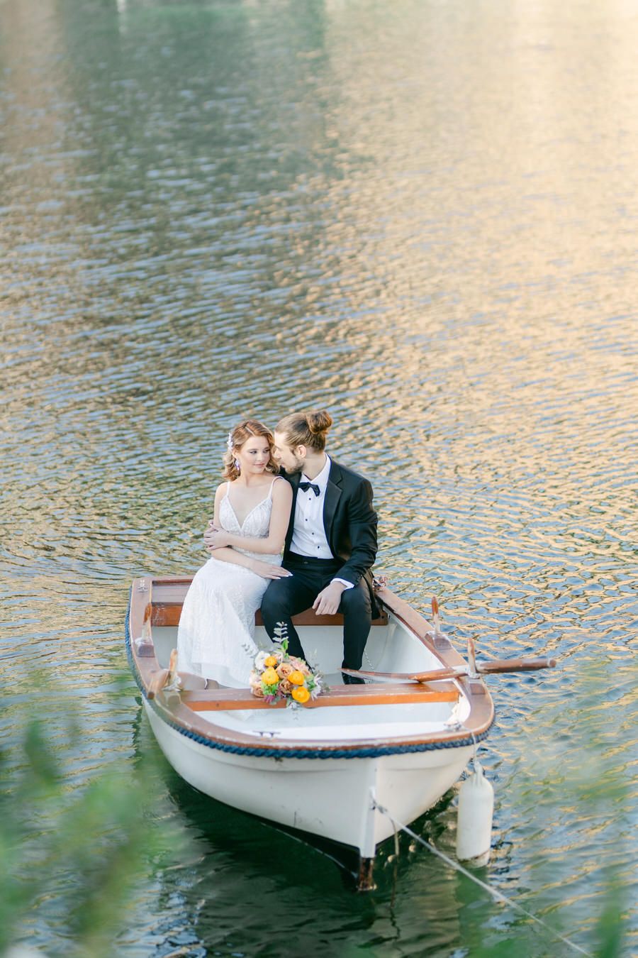 A couple sits romantically in a small wooden boat on shimmering water.