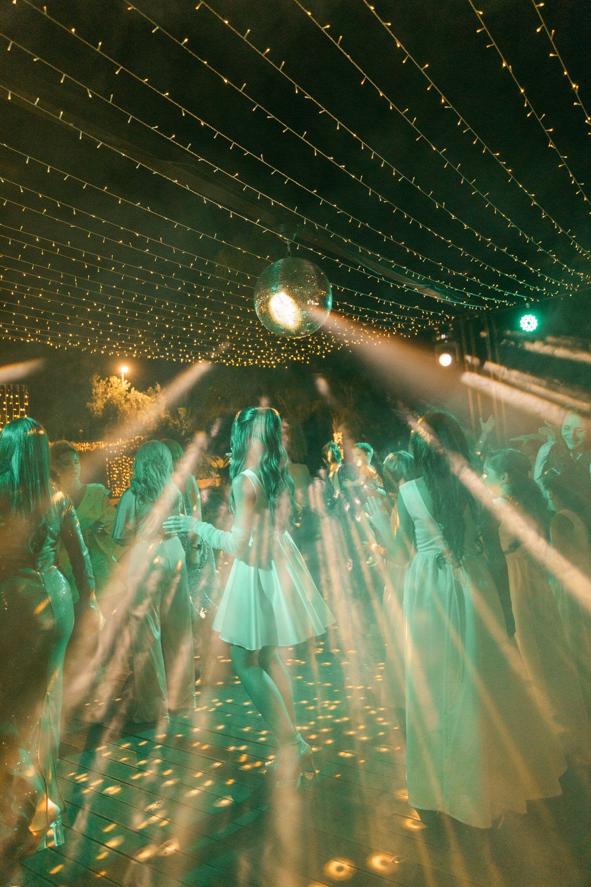 Wedding reception dance floor illuminated with string lights and beams creating ethereal turquoise atmosphere.