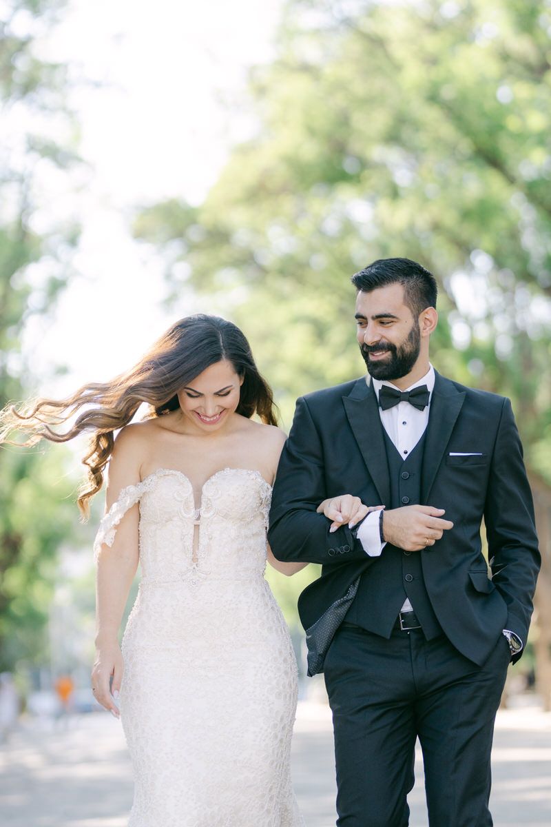 A couple in wedding attire walking together outdoors with the bride's hair flowing in the breeze.