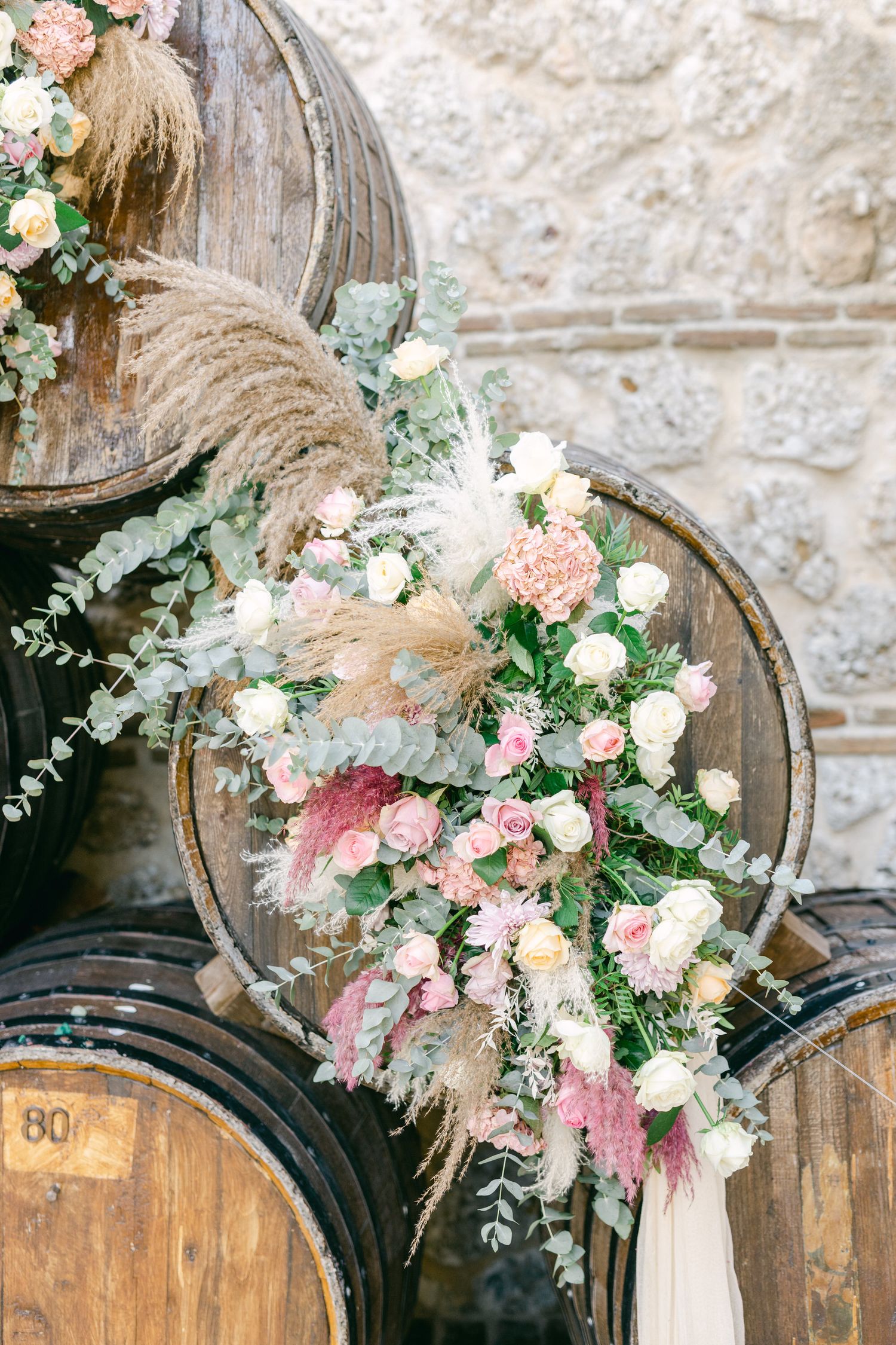 Romantic floral arrangement with pampas grass and roses decorating vintage wine barrels.