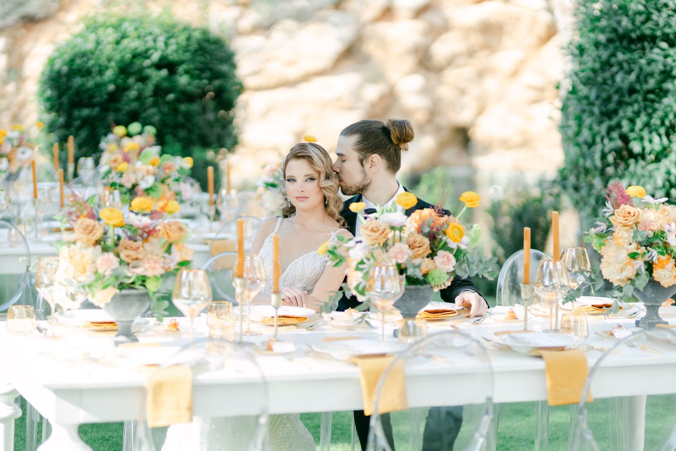 An outdoor wedding reception table decorated with peach and yellow florals and taper candles.