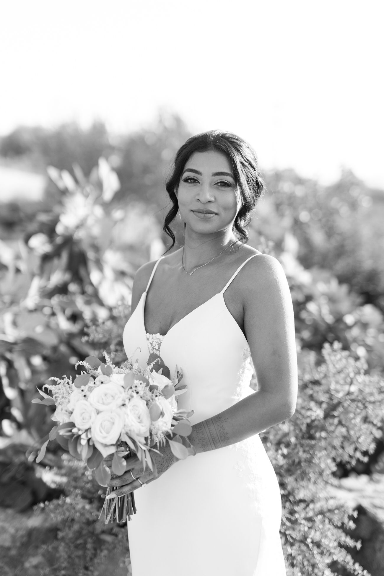 Black and white portrait of woman in spaghetti strap wedding dress holding a floral bouquet.