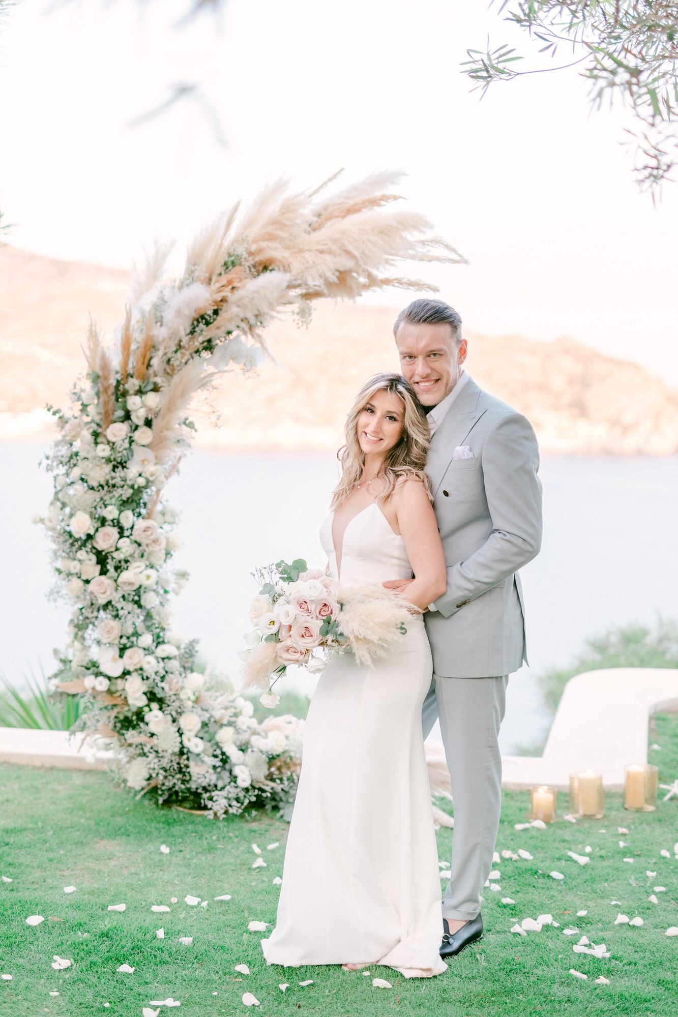 A wedding portrait under a floral arch with pampas grass and white flowers.