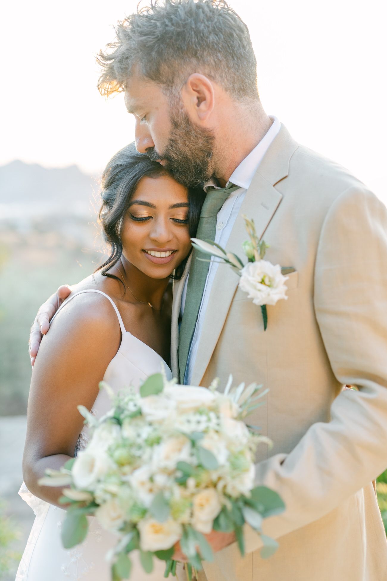 A romantic wedding photo outdoors with a delicate white bouquet and mountain landscape in the background.