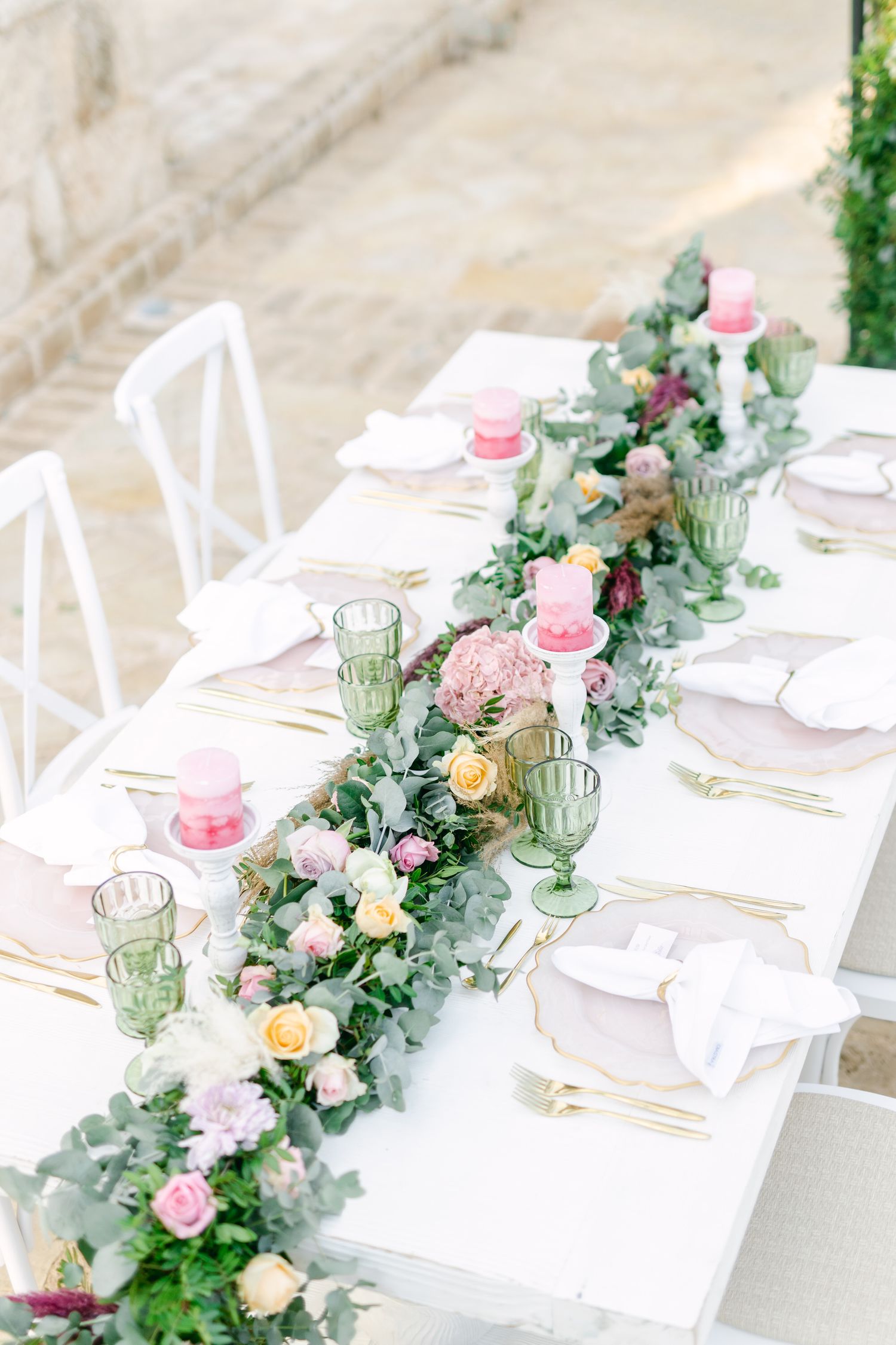 Long white wedding table decorated with pink roses and green eucalyptus.
