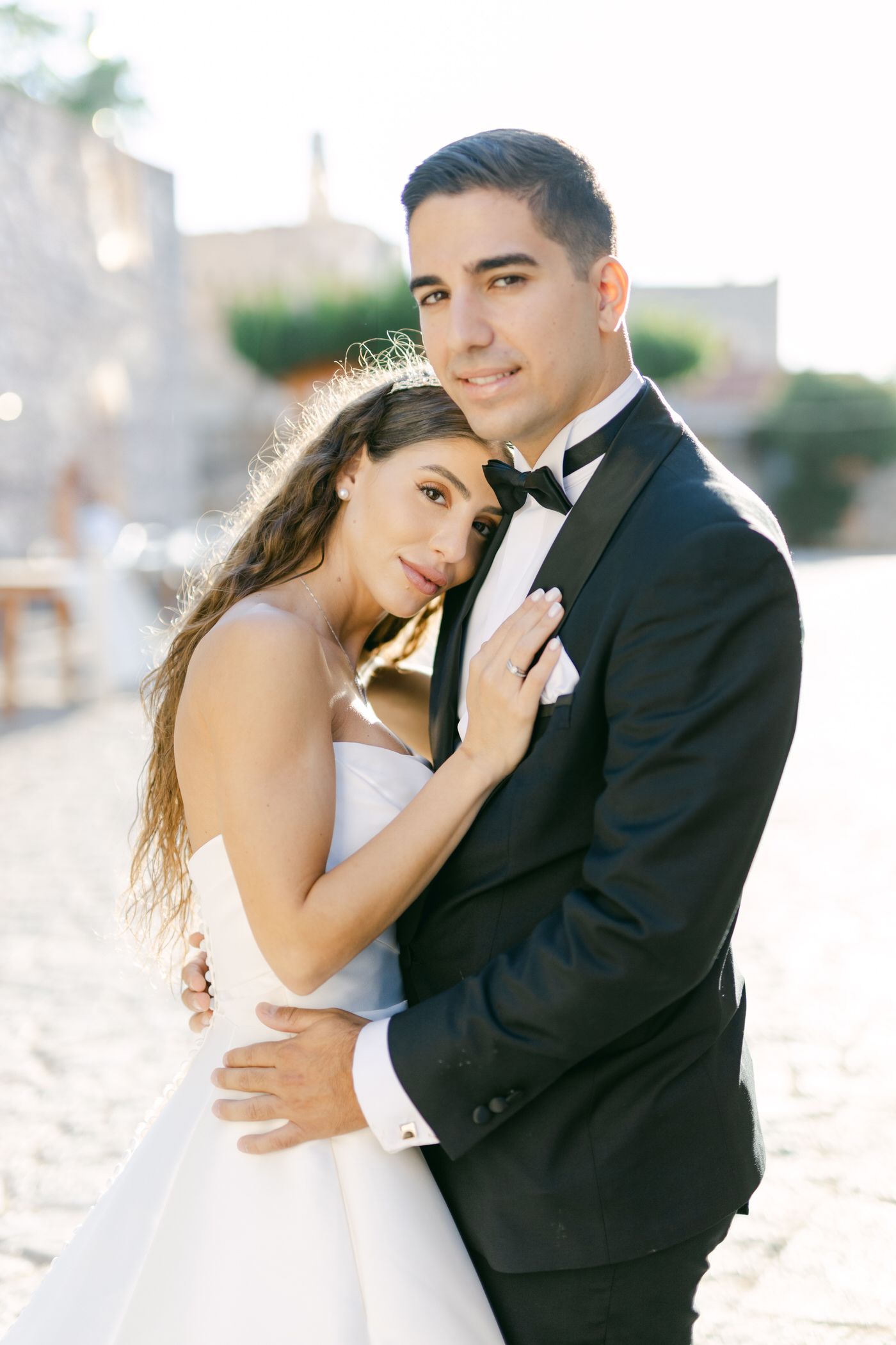 A romantic wedding portrait of a couple in formal attire embracing outdoors in soft lighting.
