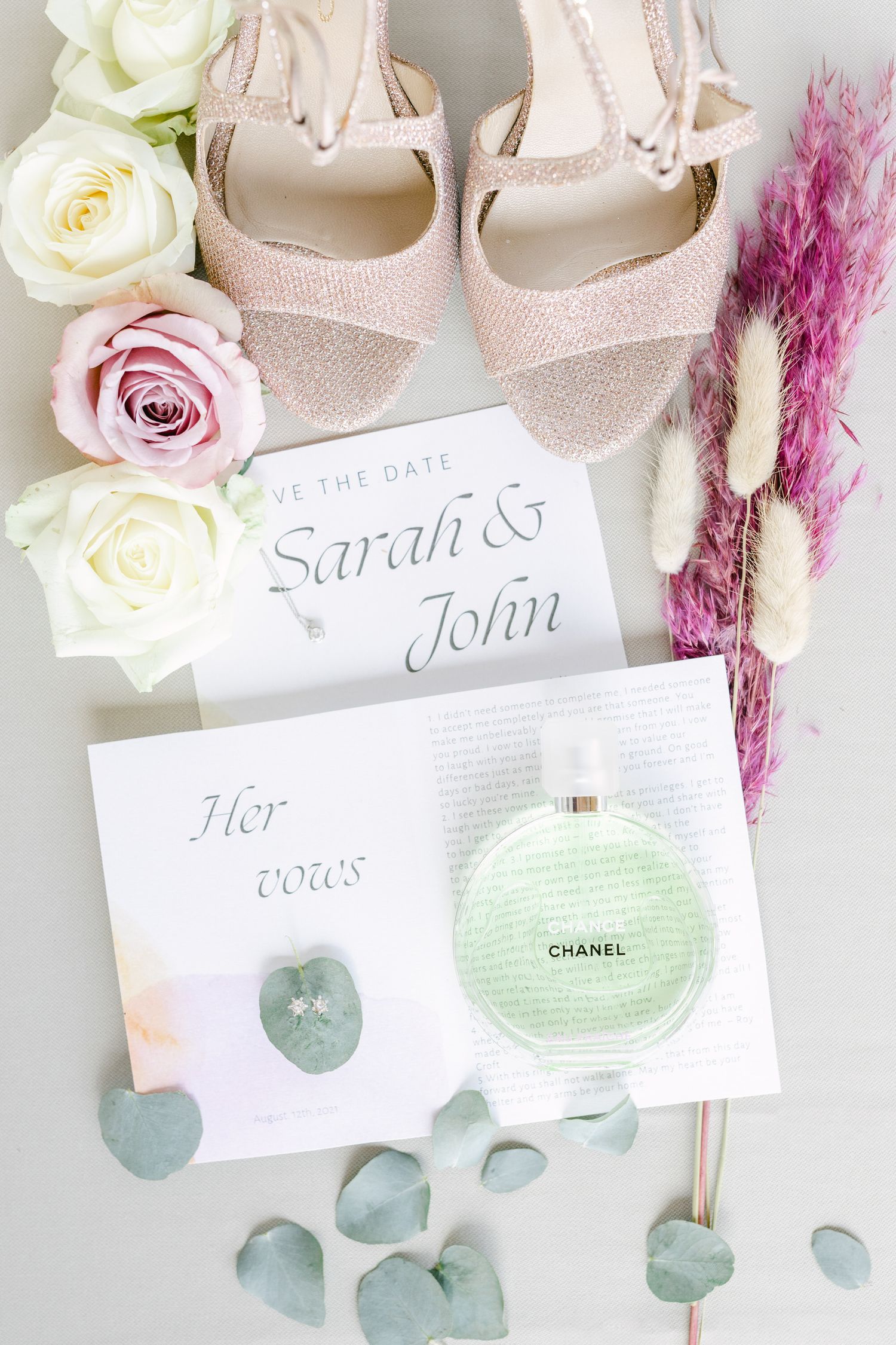 Wedding details featuring sparkly pink shoes, roses, and invitation cards with eucalyptus leaves.